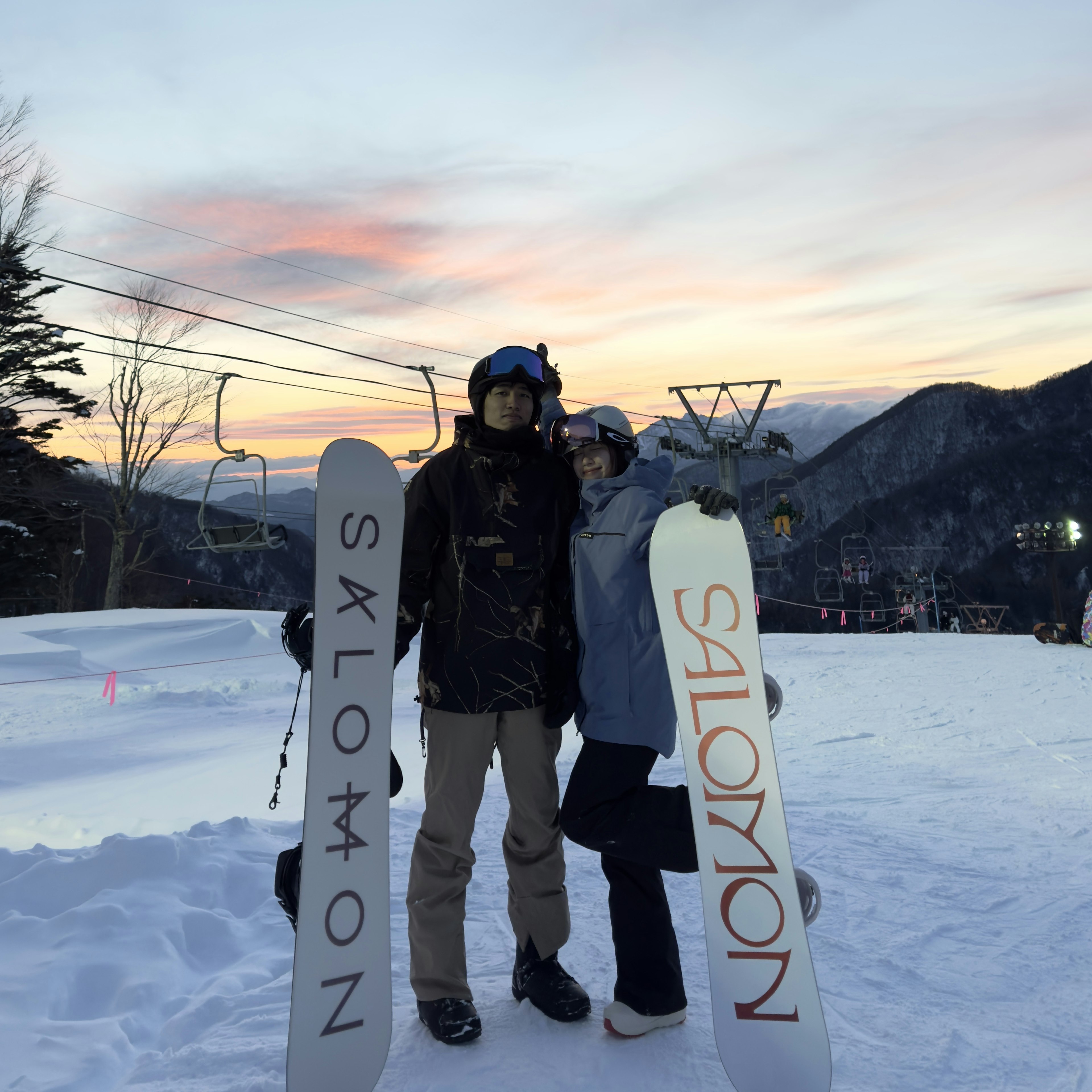 スノーボードを持ったカップルが雪の中に立っている夕焼けの景色