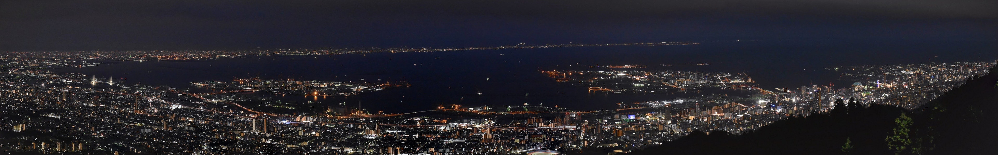 Panoramablick bei Nacht auf eine Stadt mit hellen Lichtern und Ozean