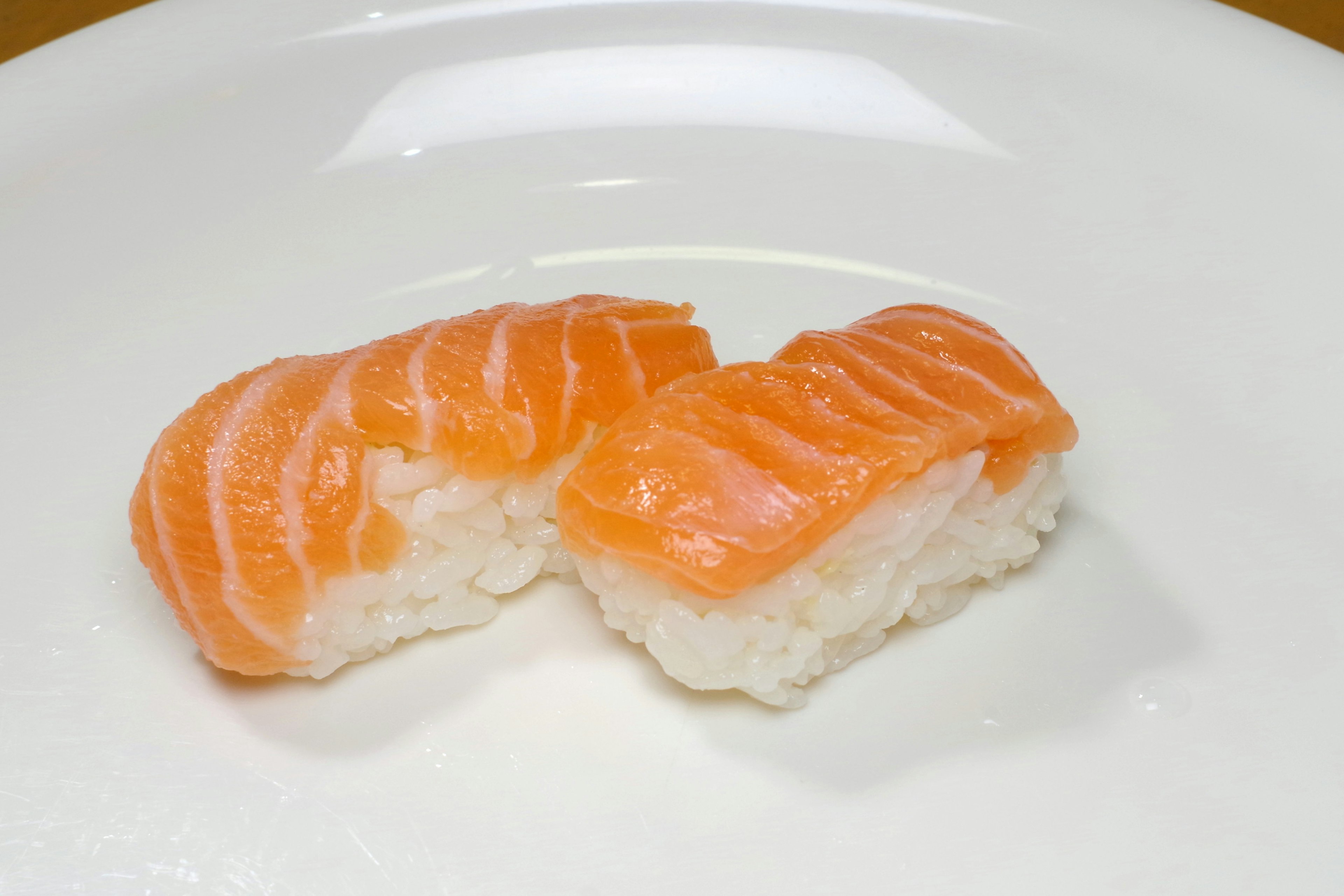 Two pieces of salmon sushi on a white plate