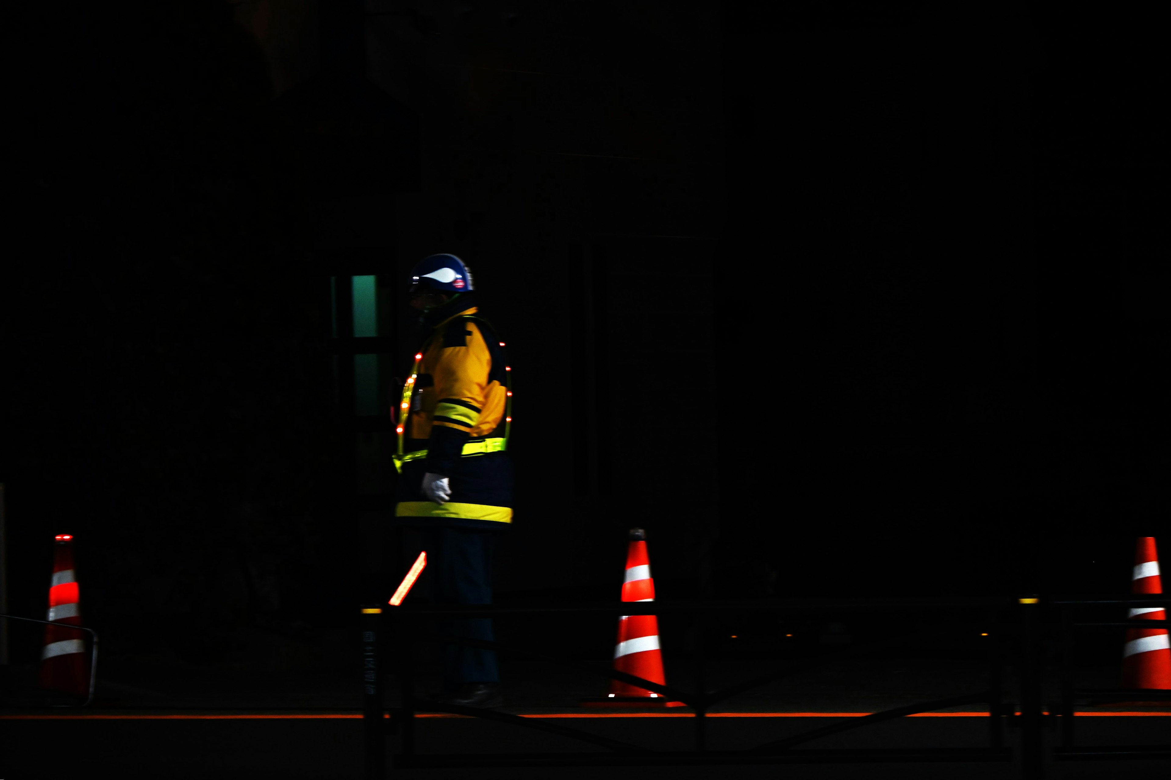 Worker wearing reflective vest in dark background with traffic cones