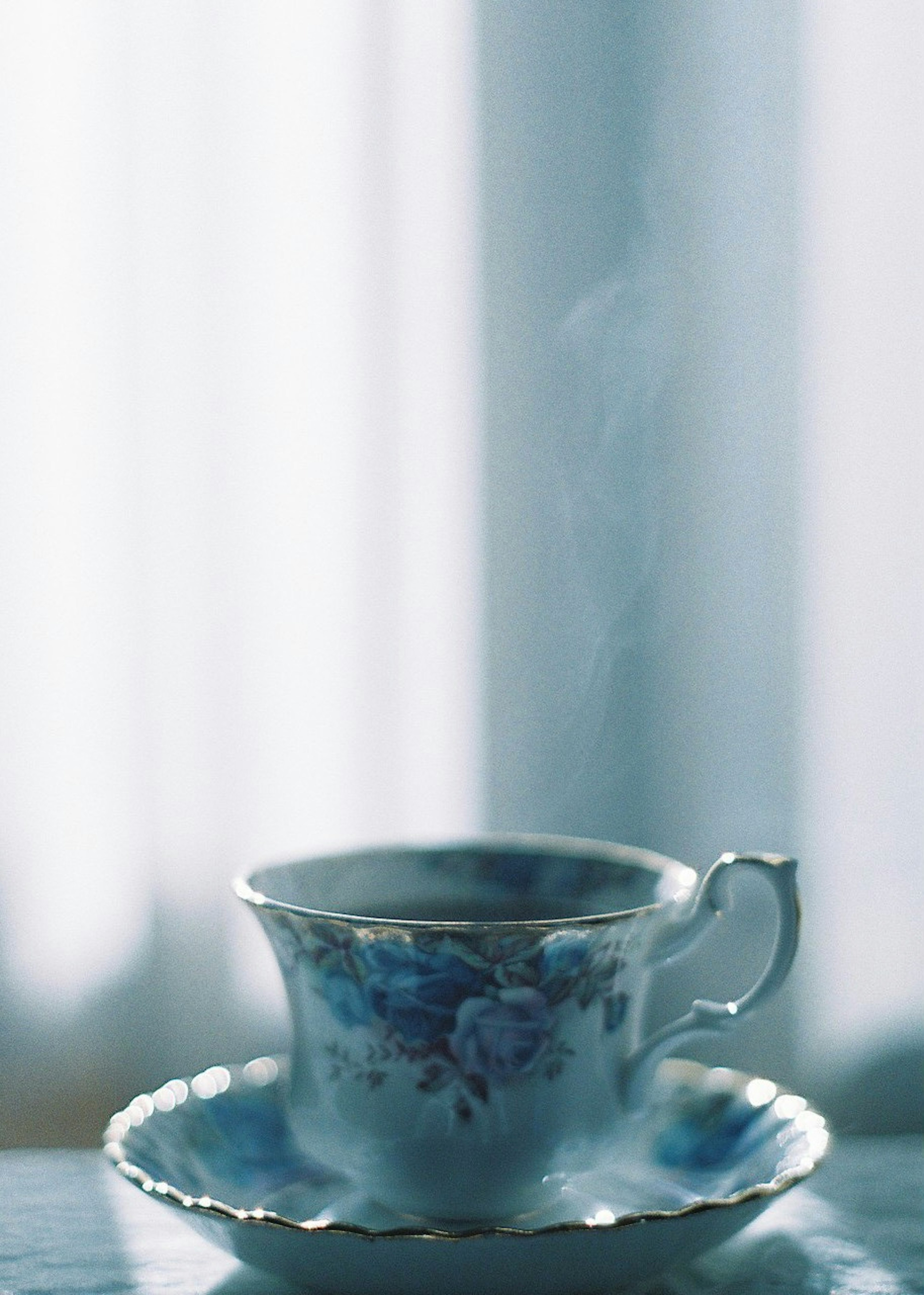 Blue floral patterned teacup and saucer steam rising soft background