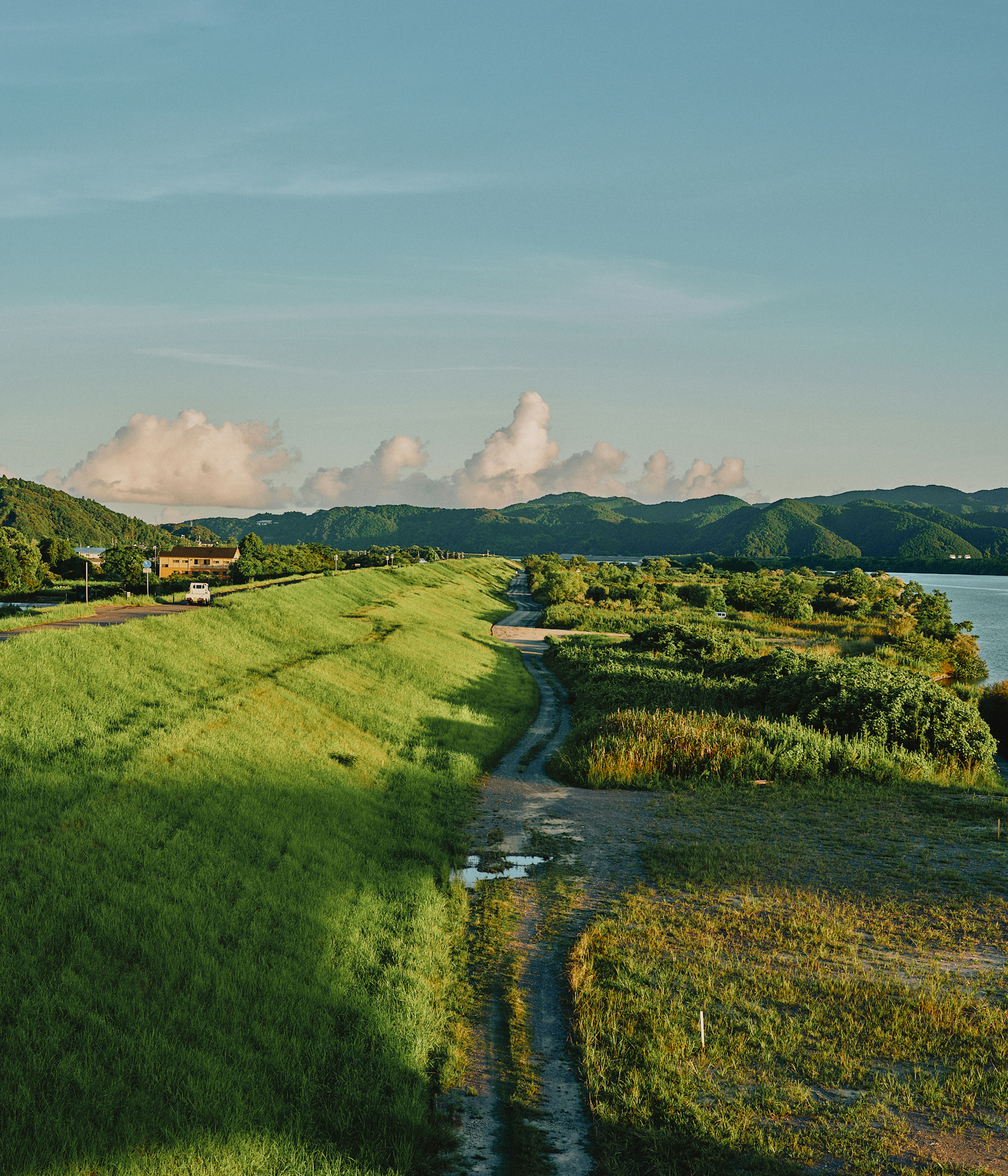 Lush green landscape under a blue sky with distant mountains and white clouds