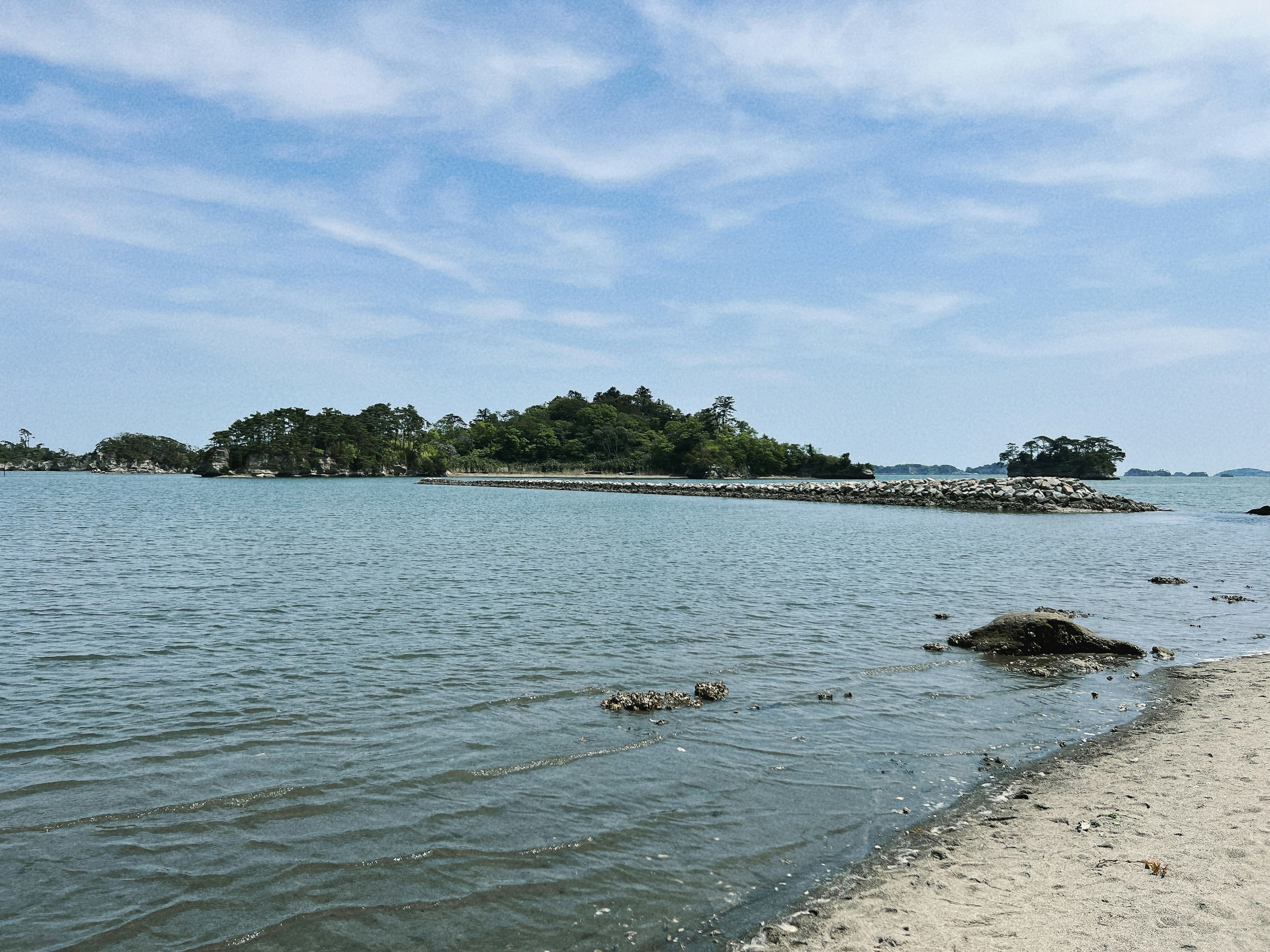 ทิวทัศน์ชายหาดที่เงียบสงบ มีน้ำที่สงบ เกาะเล็ก ๆ และท้องฟ้าสีฟ้า