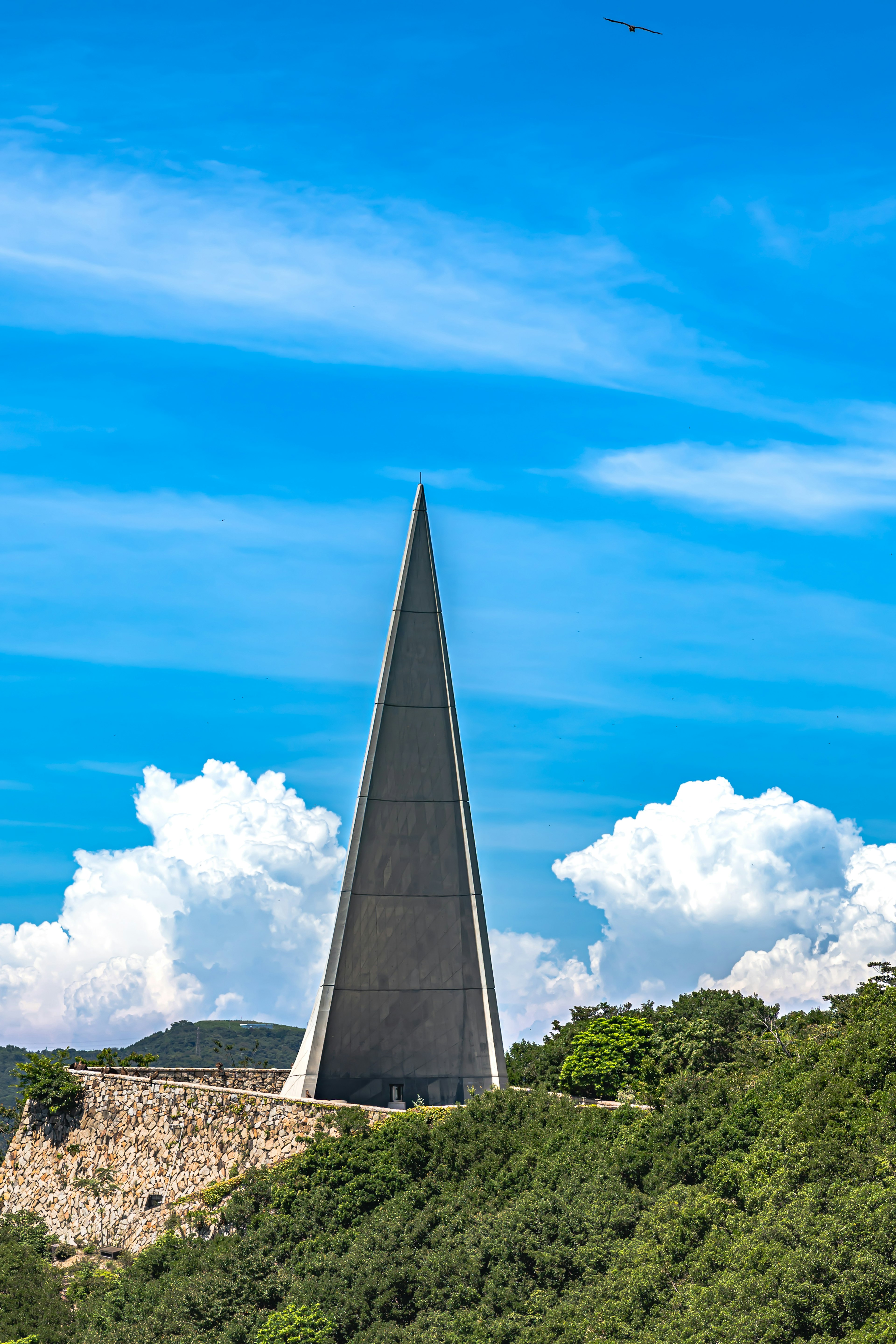 Una estructura arquitectónica puntiaguda contra un cielo azul brillante con nubes esponjosas y un paisaje verde