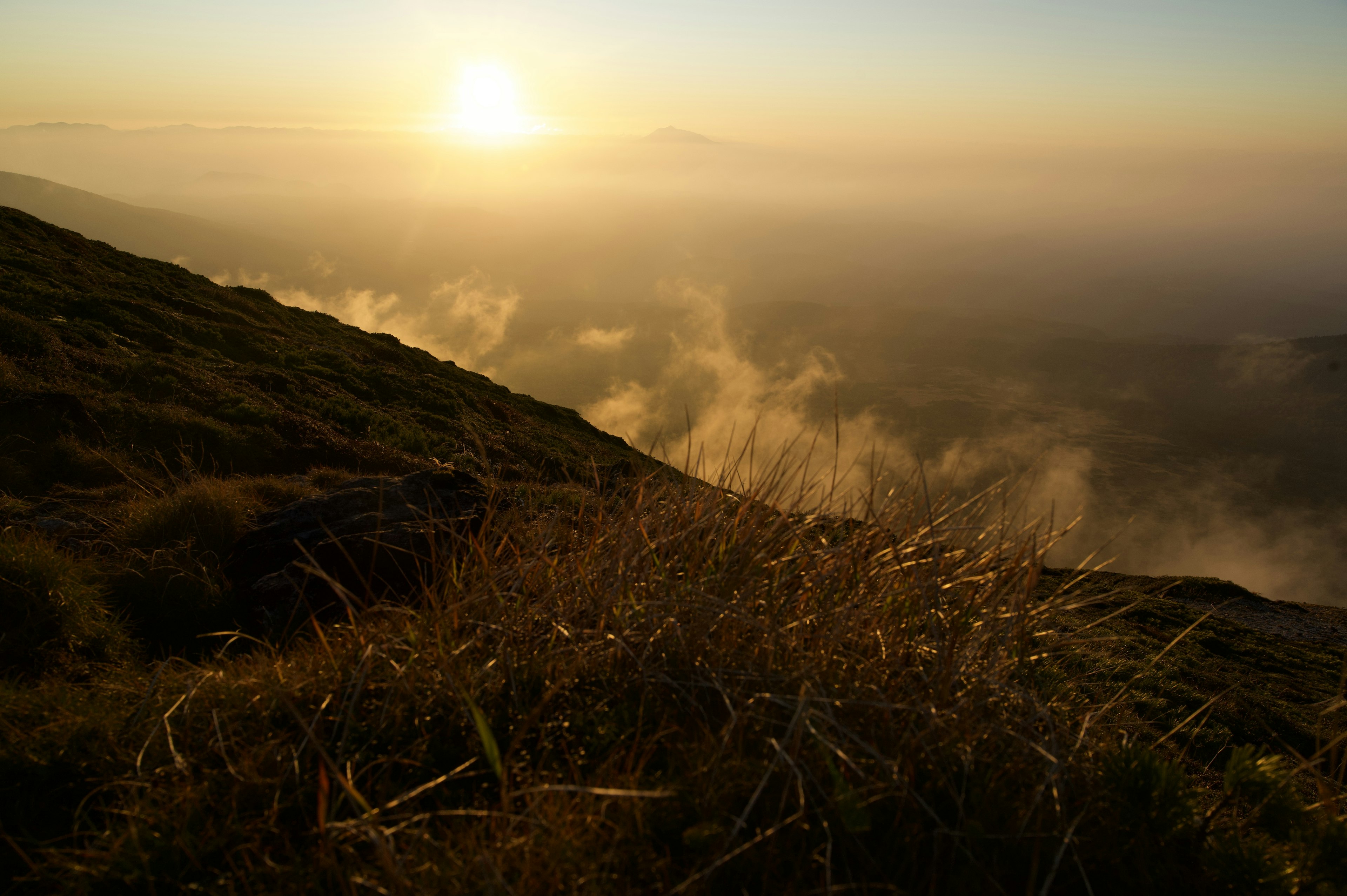 Lever de soleil sur un paysage montagneux avec de la brume et de l'herbe