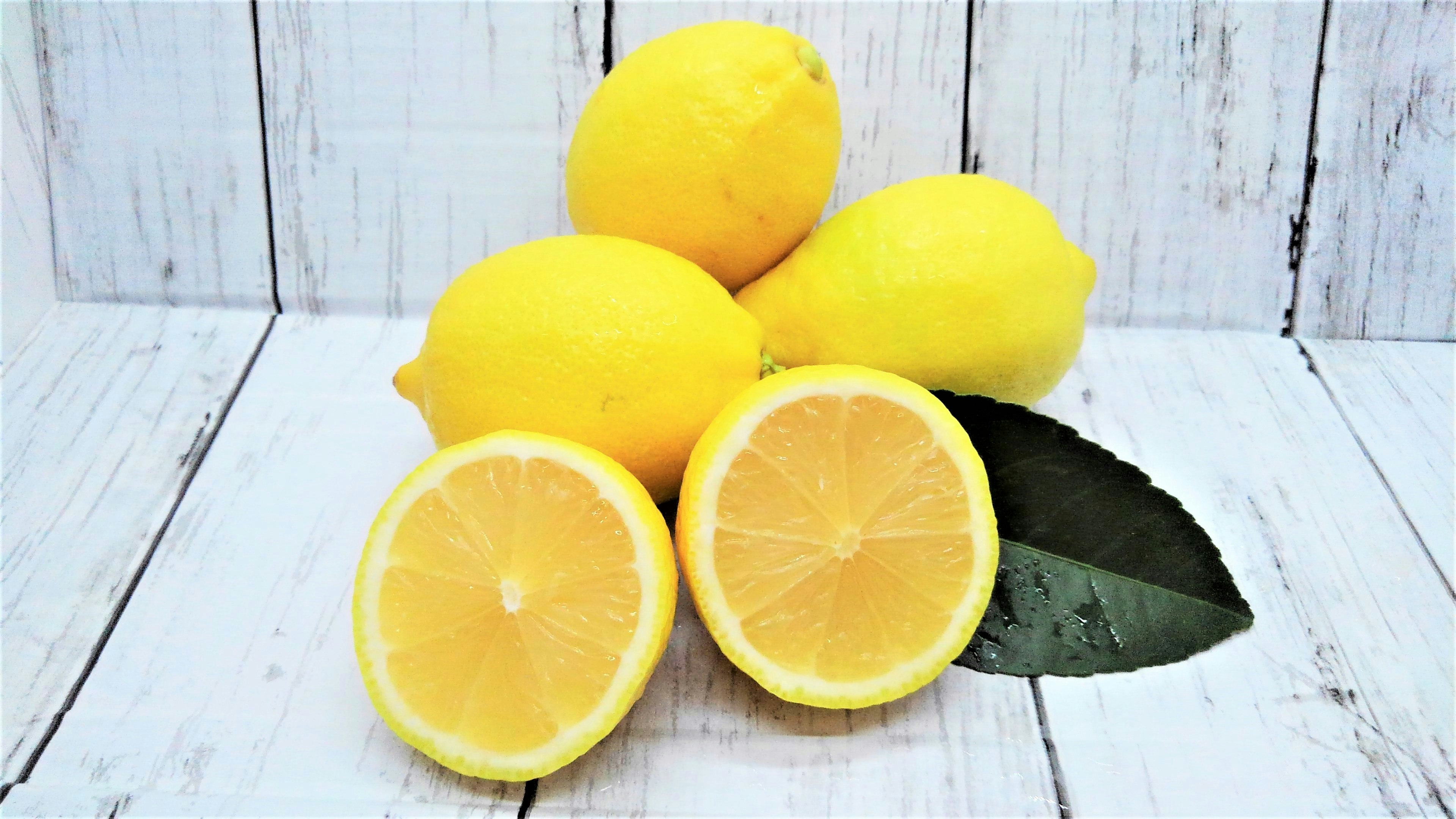 Photo de citrons jaunes et d'un citron coupé avec des feuilles vertes et un fond en bois blanc