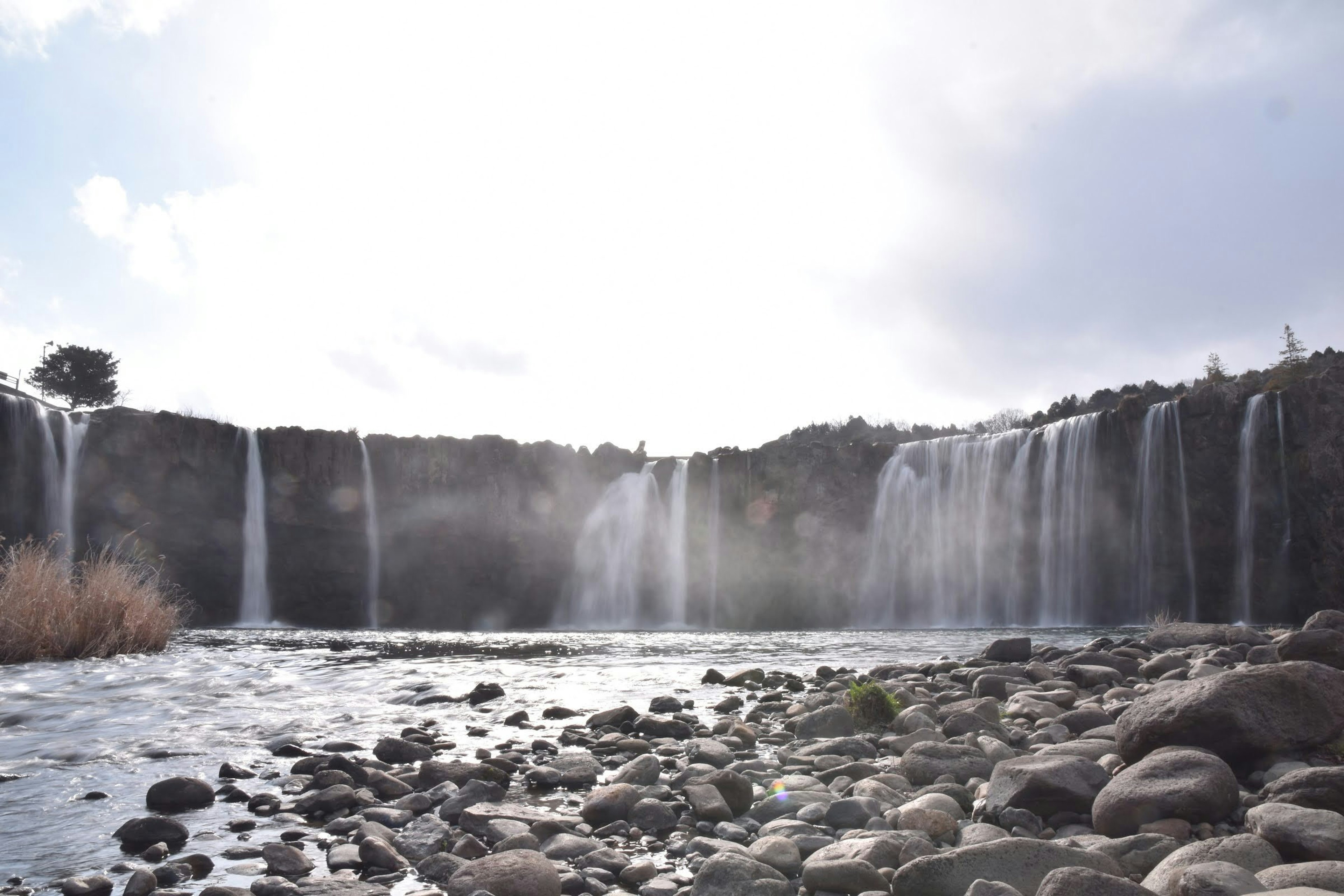 Pemandangan air terjun yang mengalir ke sungai dengan batu-batu