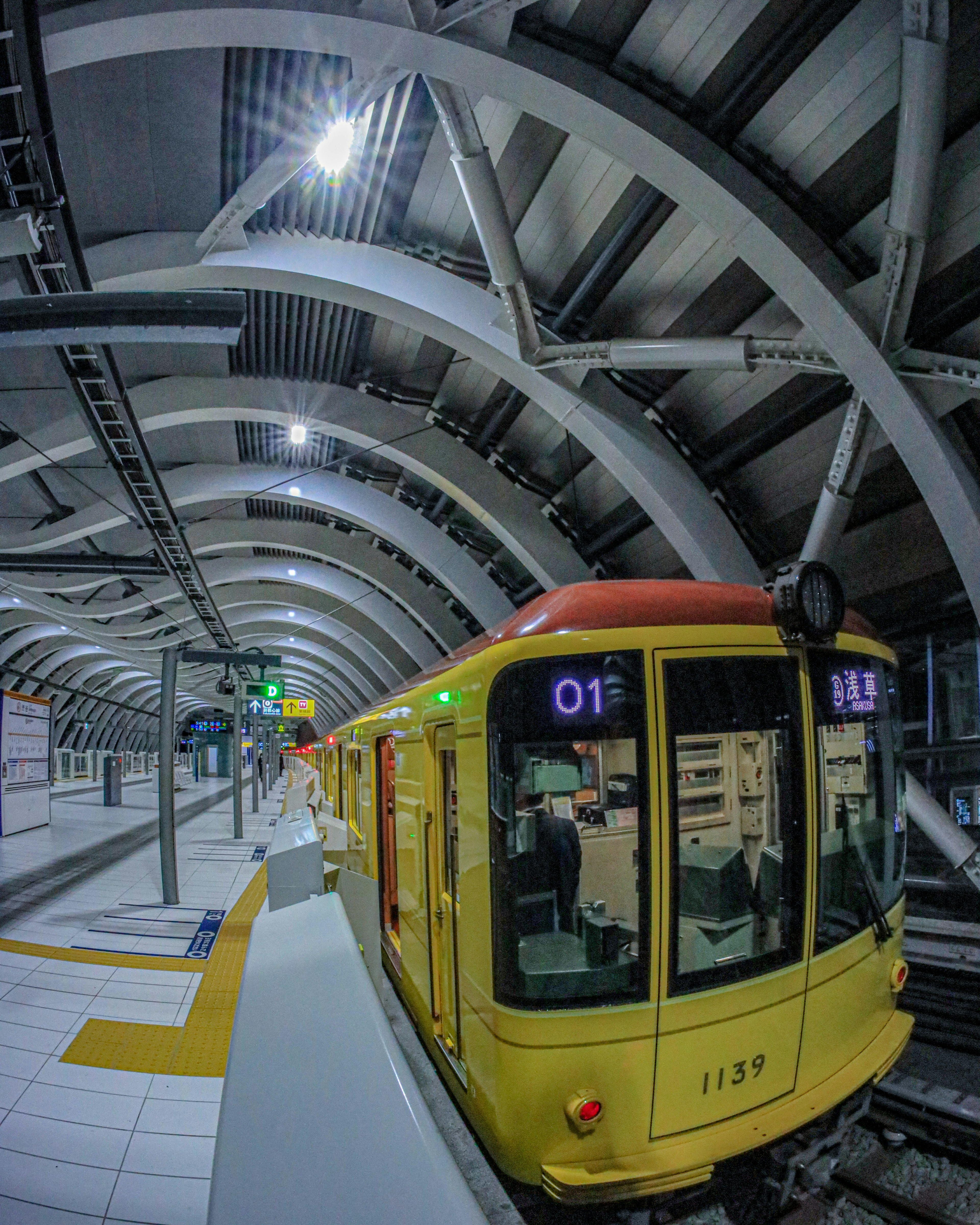 Tren amarillo en una estación moderna con arquitectura curvada y marcas de plataforma