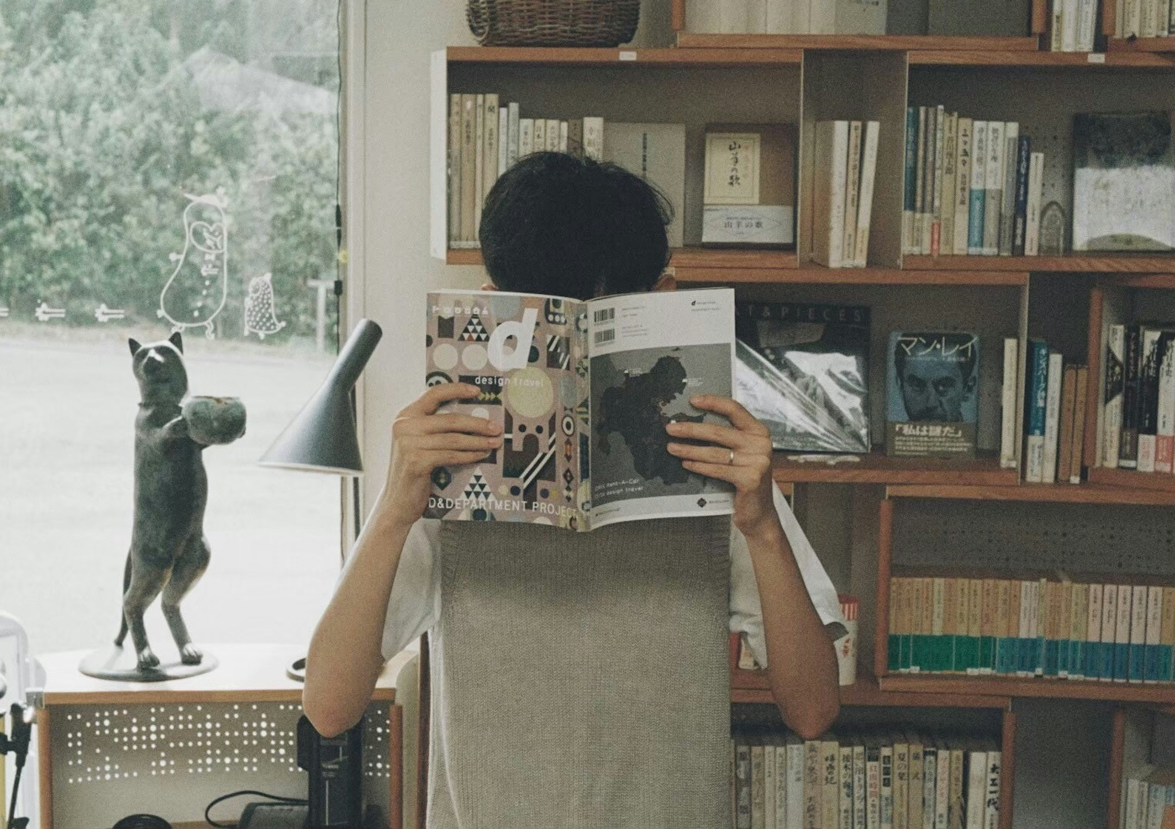 A young person holding a magazine in a cozy room with bookshelves