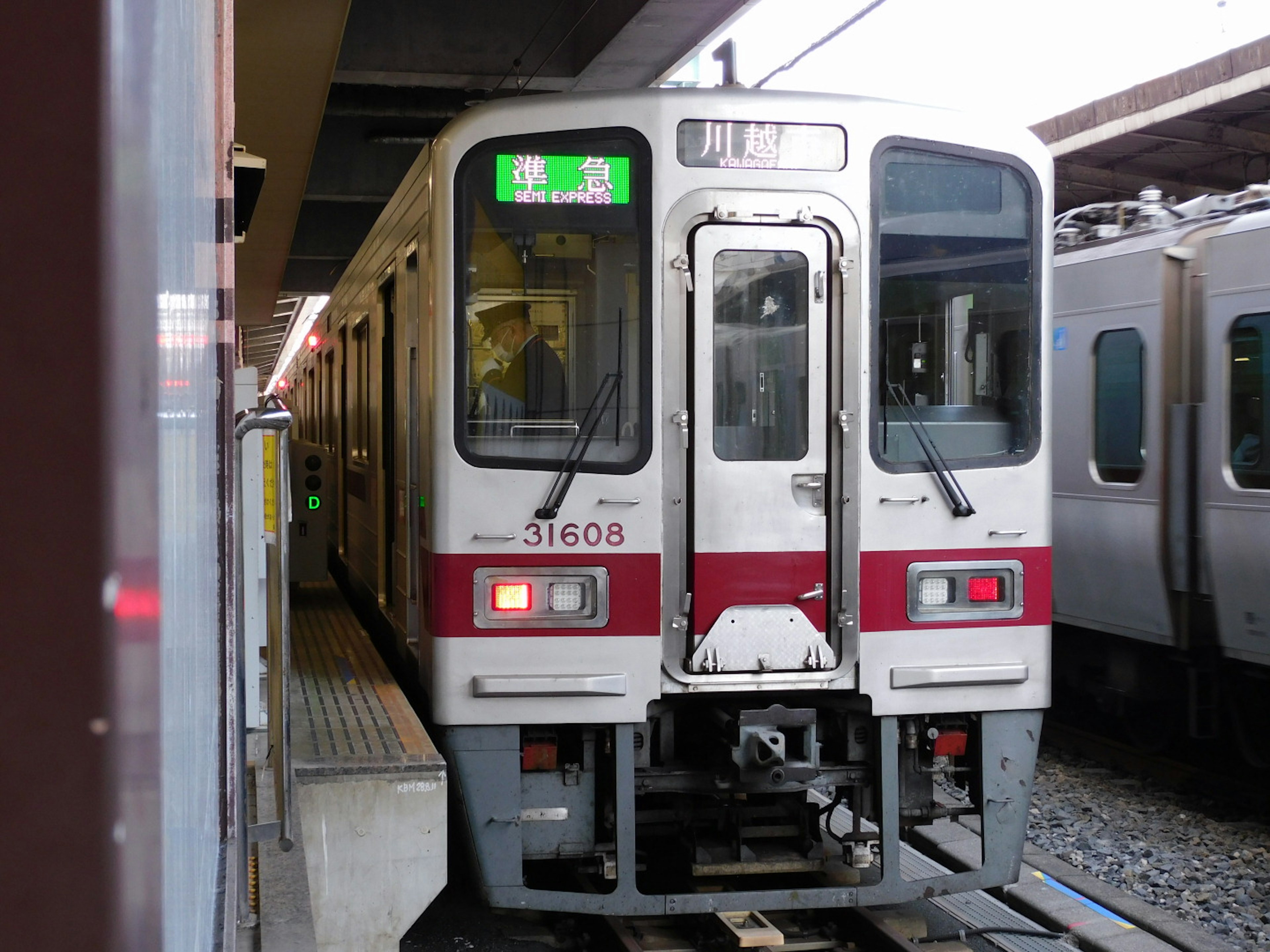 A white and red train stopped at a station with a green display visible