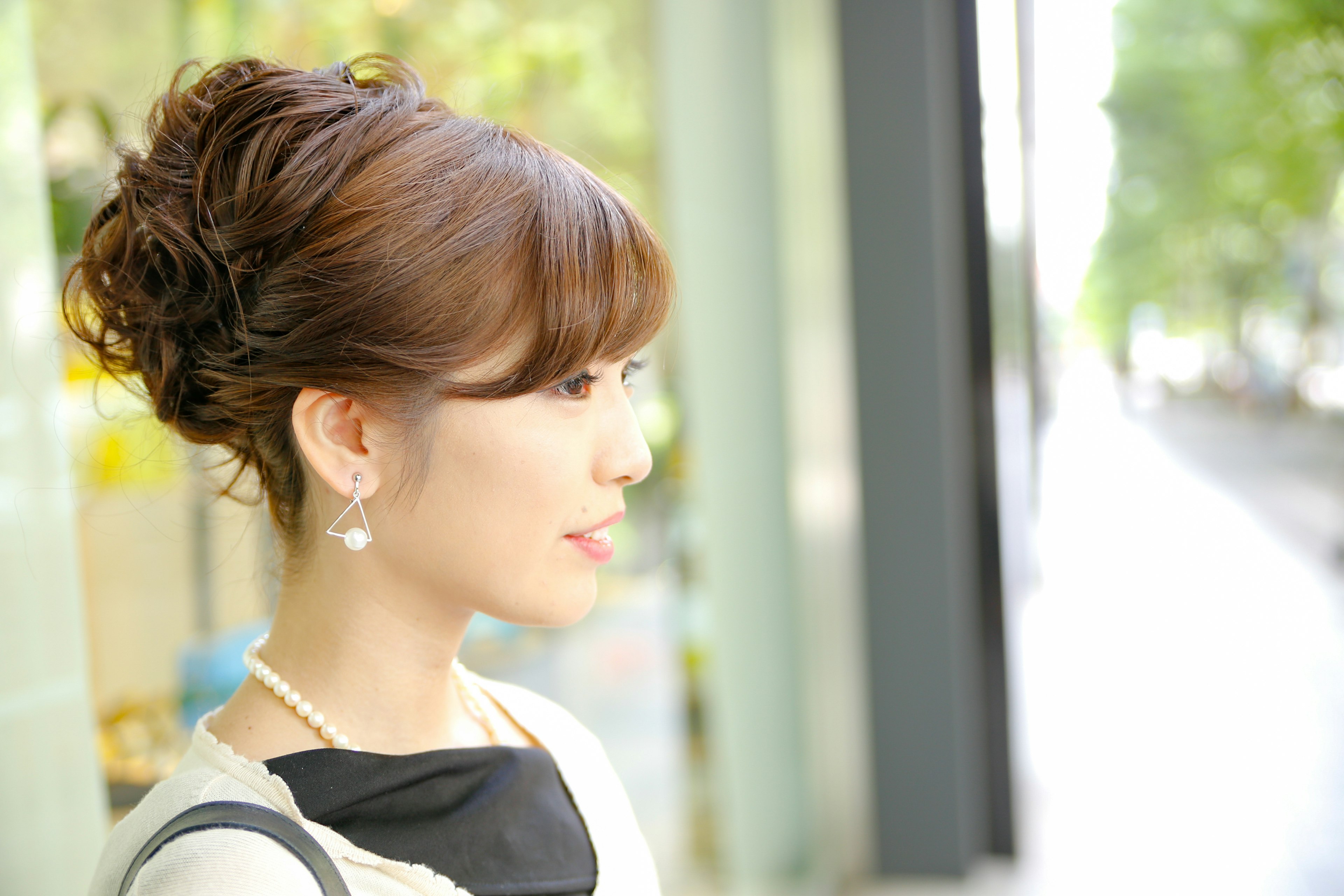 Profil d'une femme avec une coiffure relevée portant des boucles d'oreilles en perles devant un paysage urbain