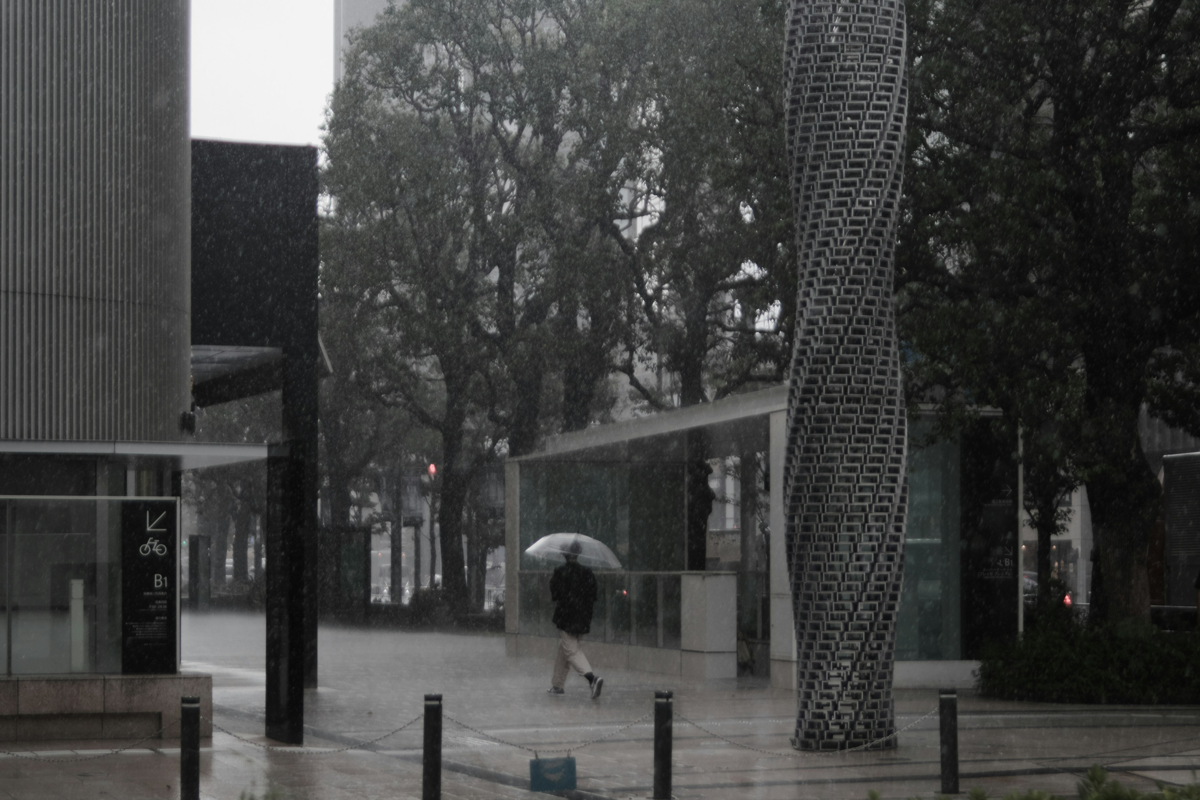 Persona caminando con un paraguas bajo la lluvia rodeada de arquitectura moderna