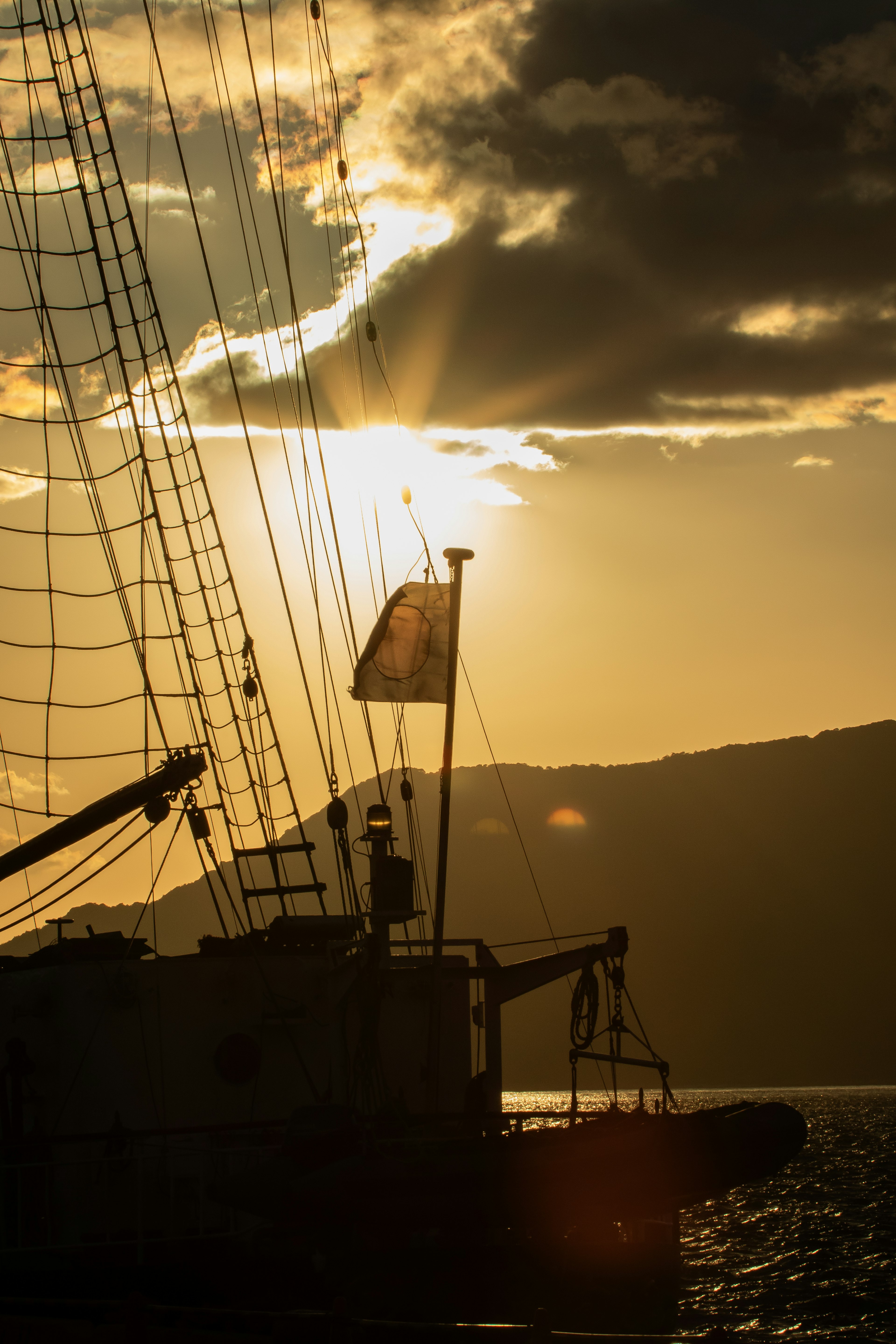 Silhouette d'un bateau à voiles contre des rayons de coucher de soleil sur l'eau