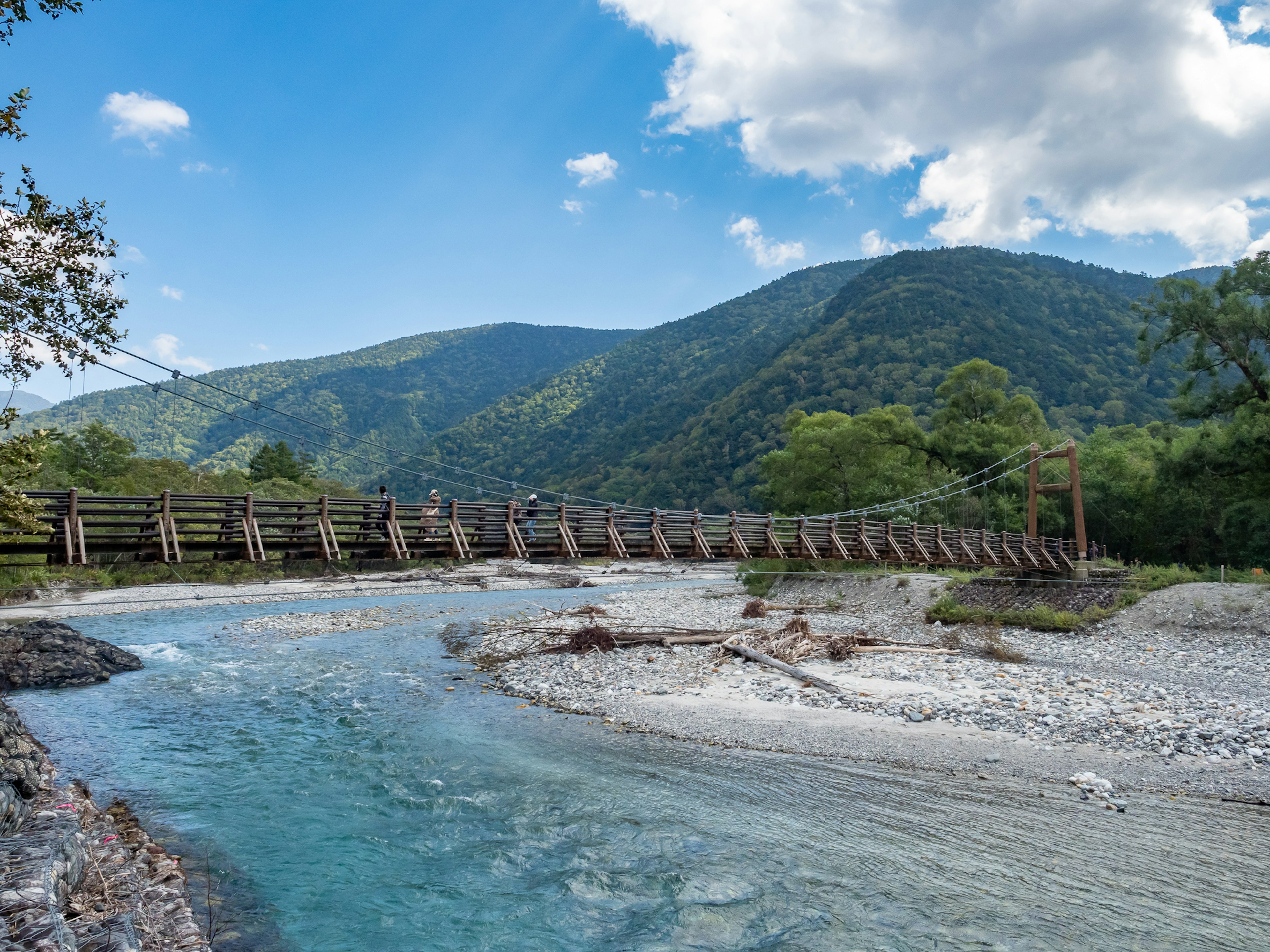 Vista escénica de montañas y un río con un puente colgante de madera