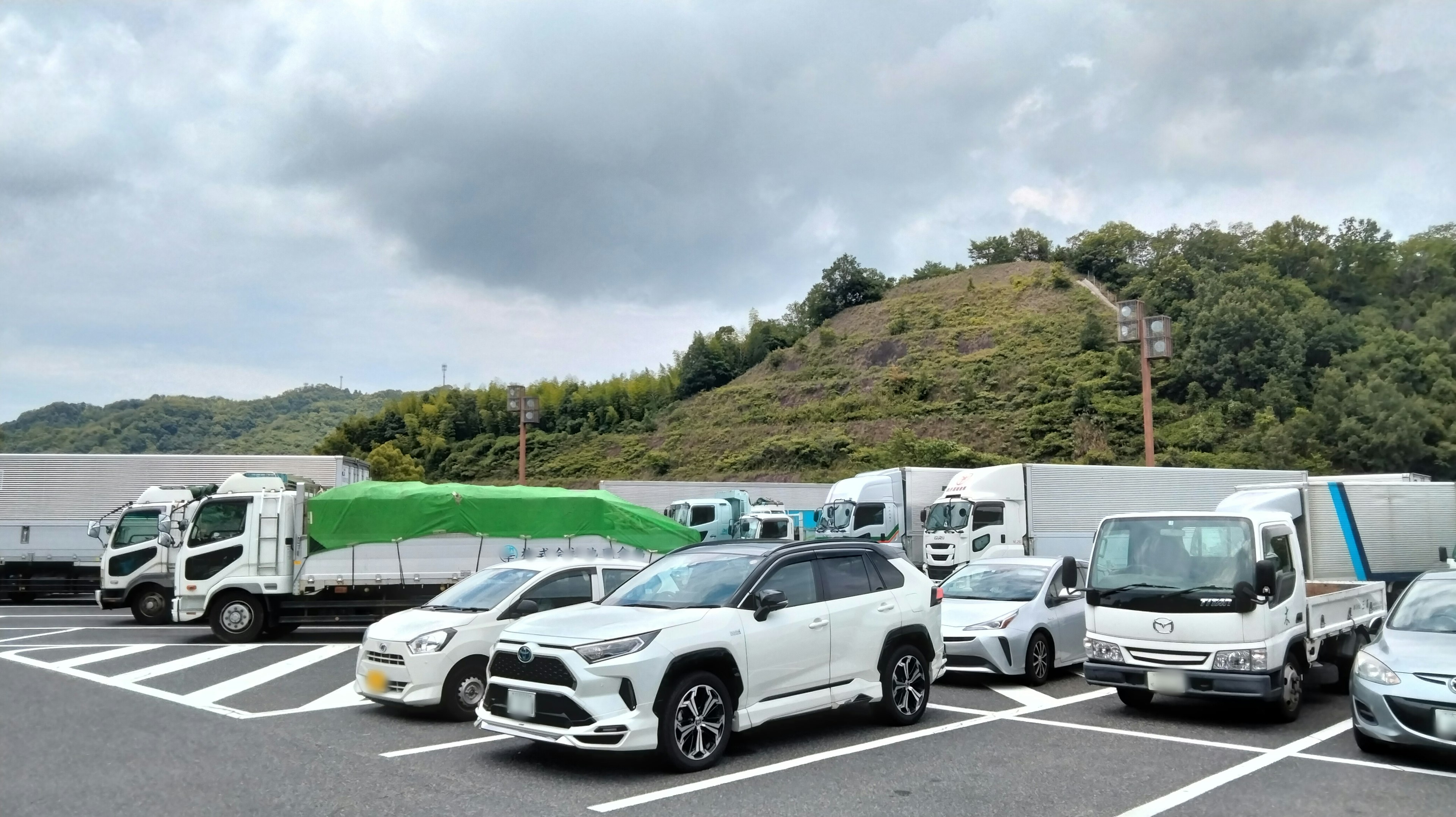 Parking lot scene with white vehicles including trucks and a hill in the background