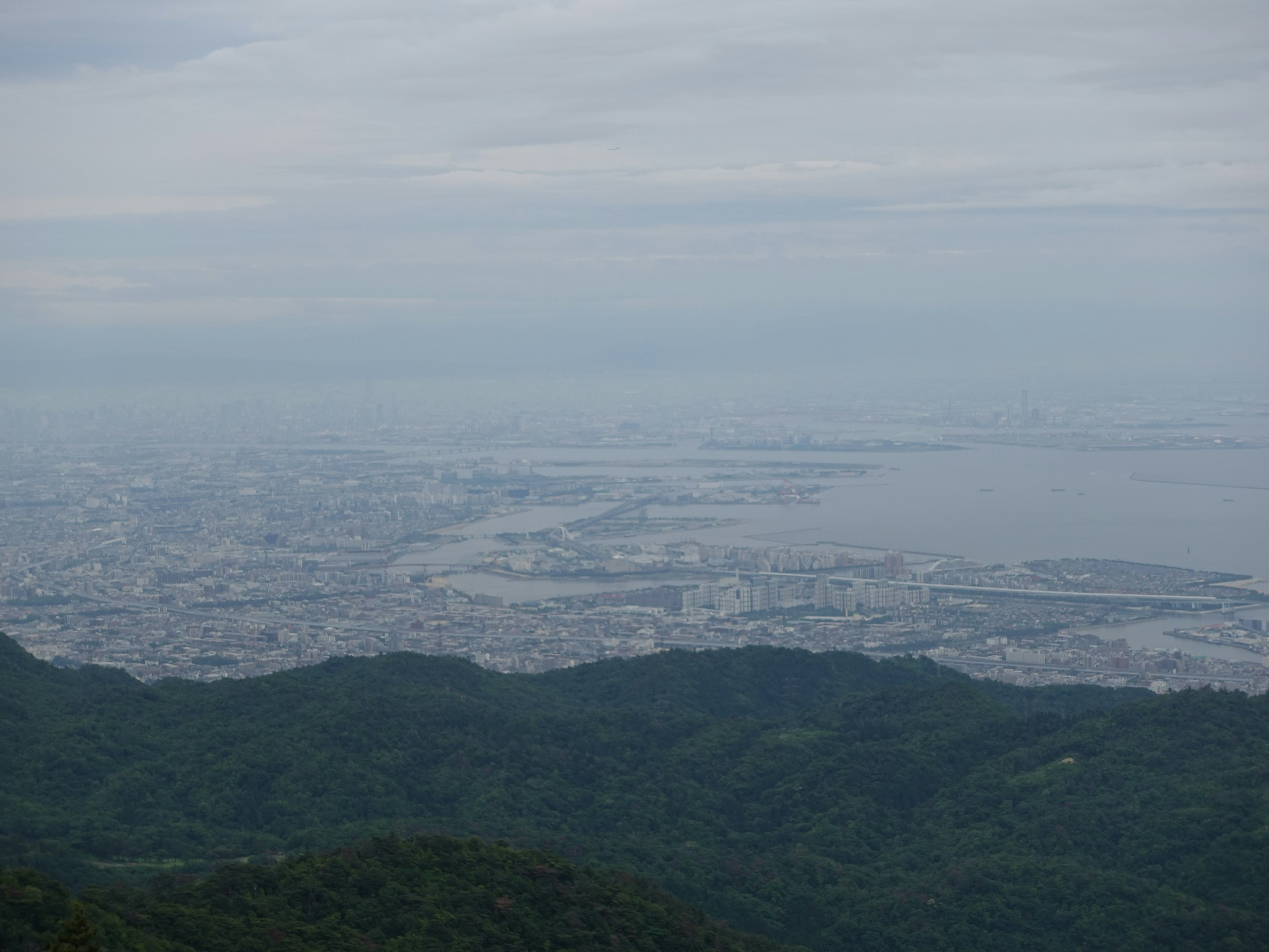 山の上から見た都市と海の景色 雲の多い空と緑の山々