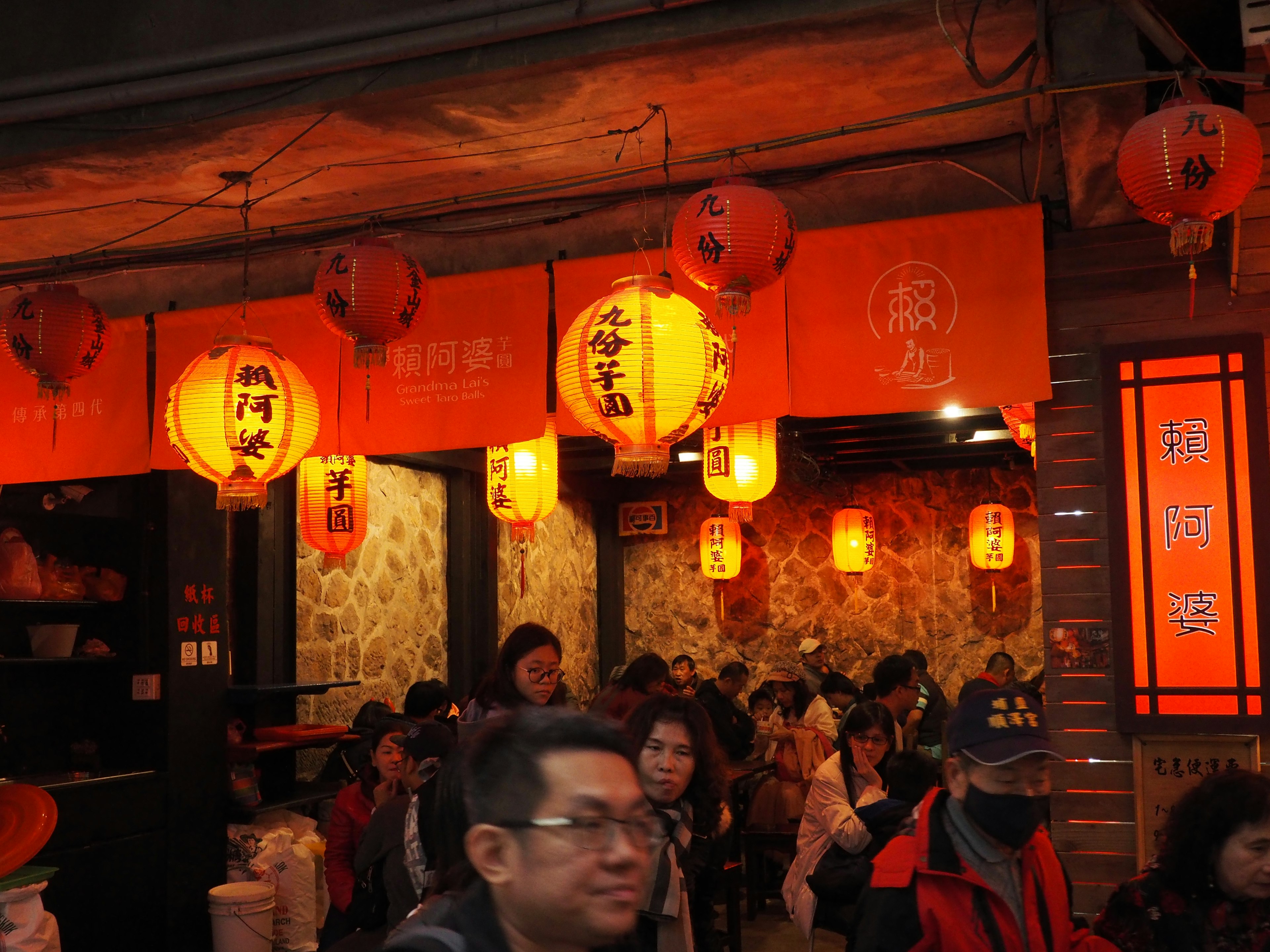 A bustling restaurant with orange lanterns and warm lighting filled with patrons