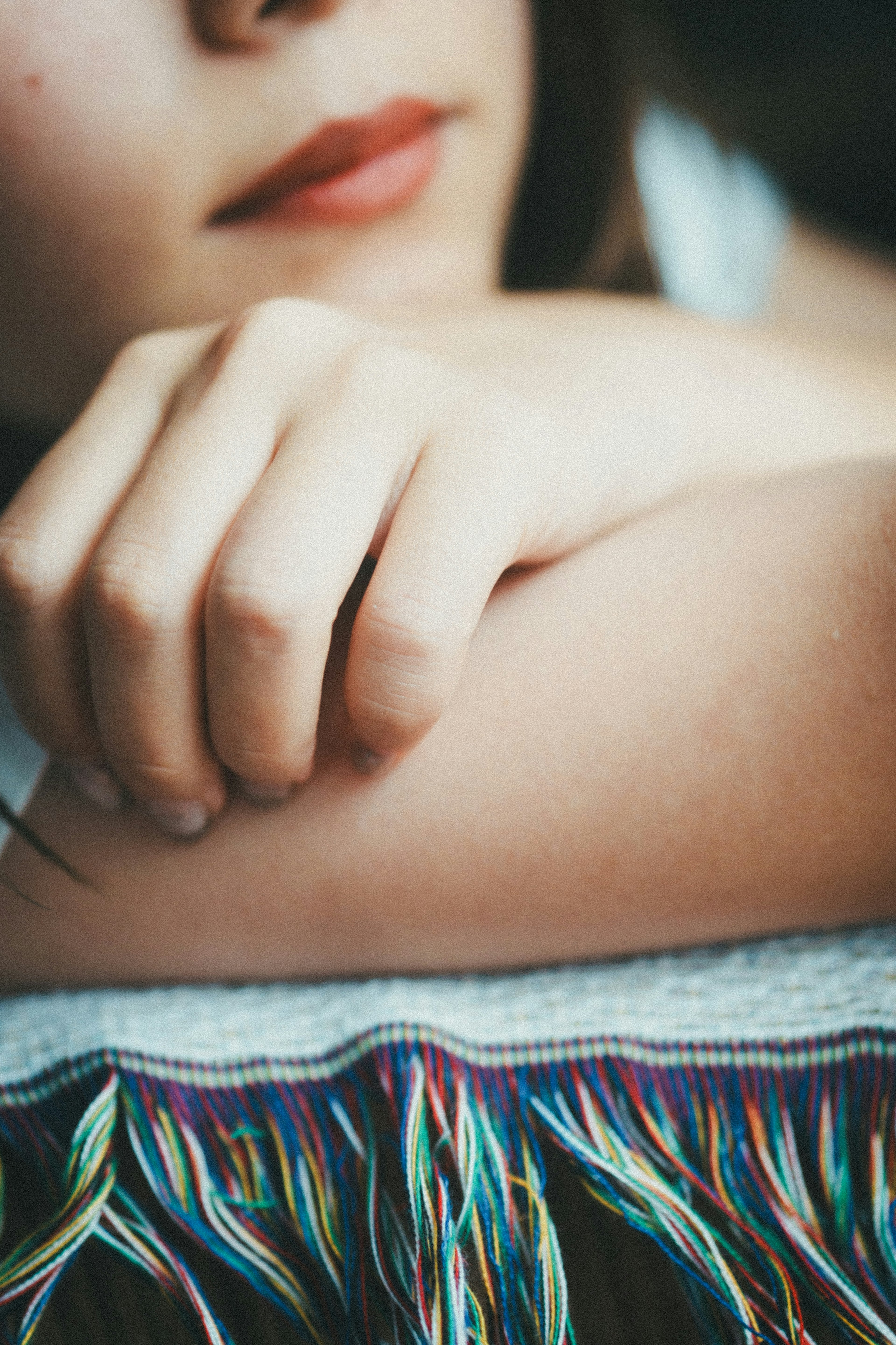 A woman's arm and hand resting on a colorful fringed textile