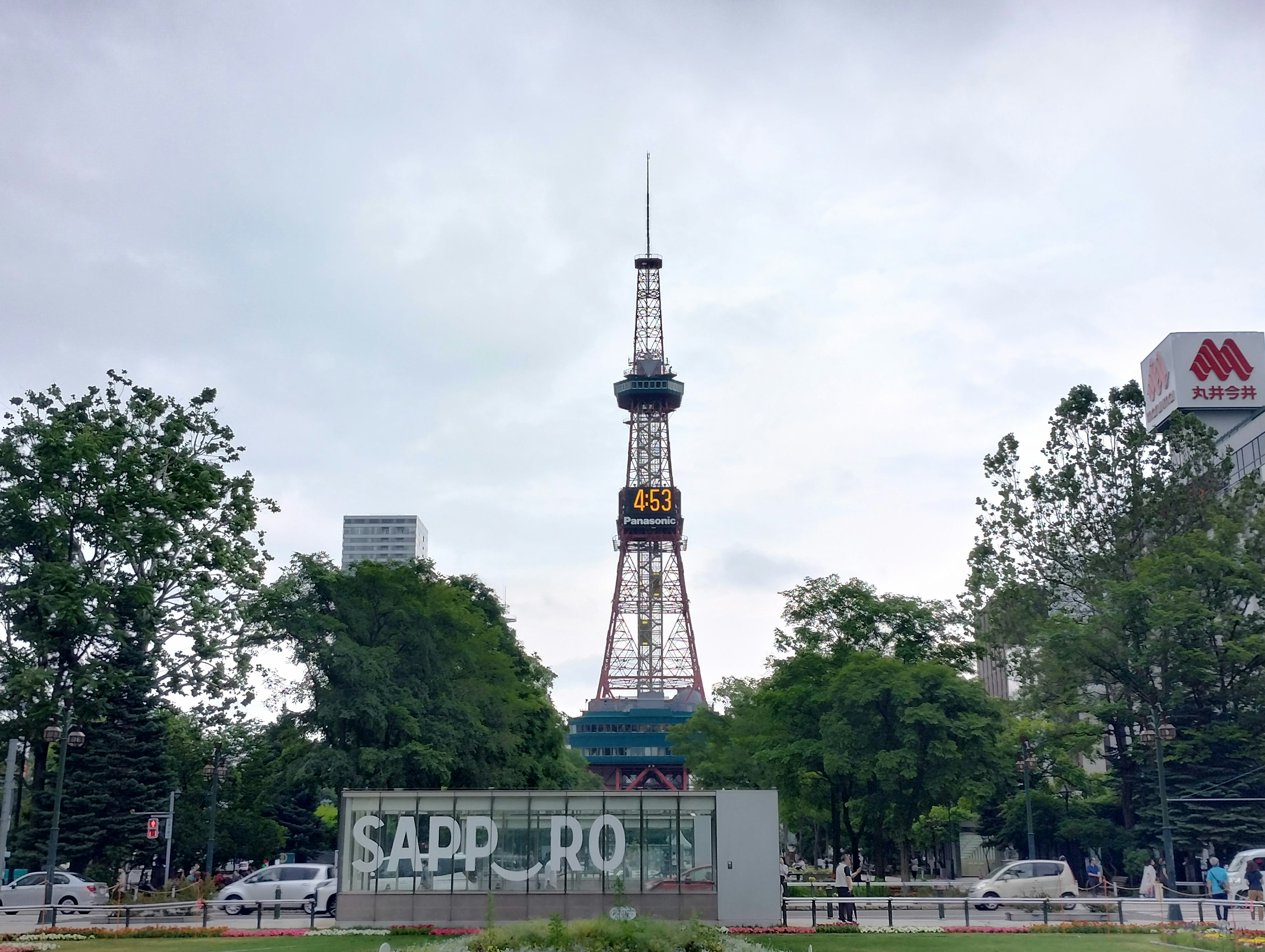 Blick auf den Sapporo Fernsehturm in einem Park mit grünen Bäumen und bewölktem Himmel