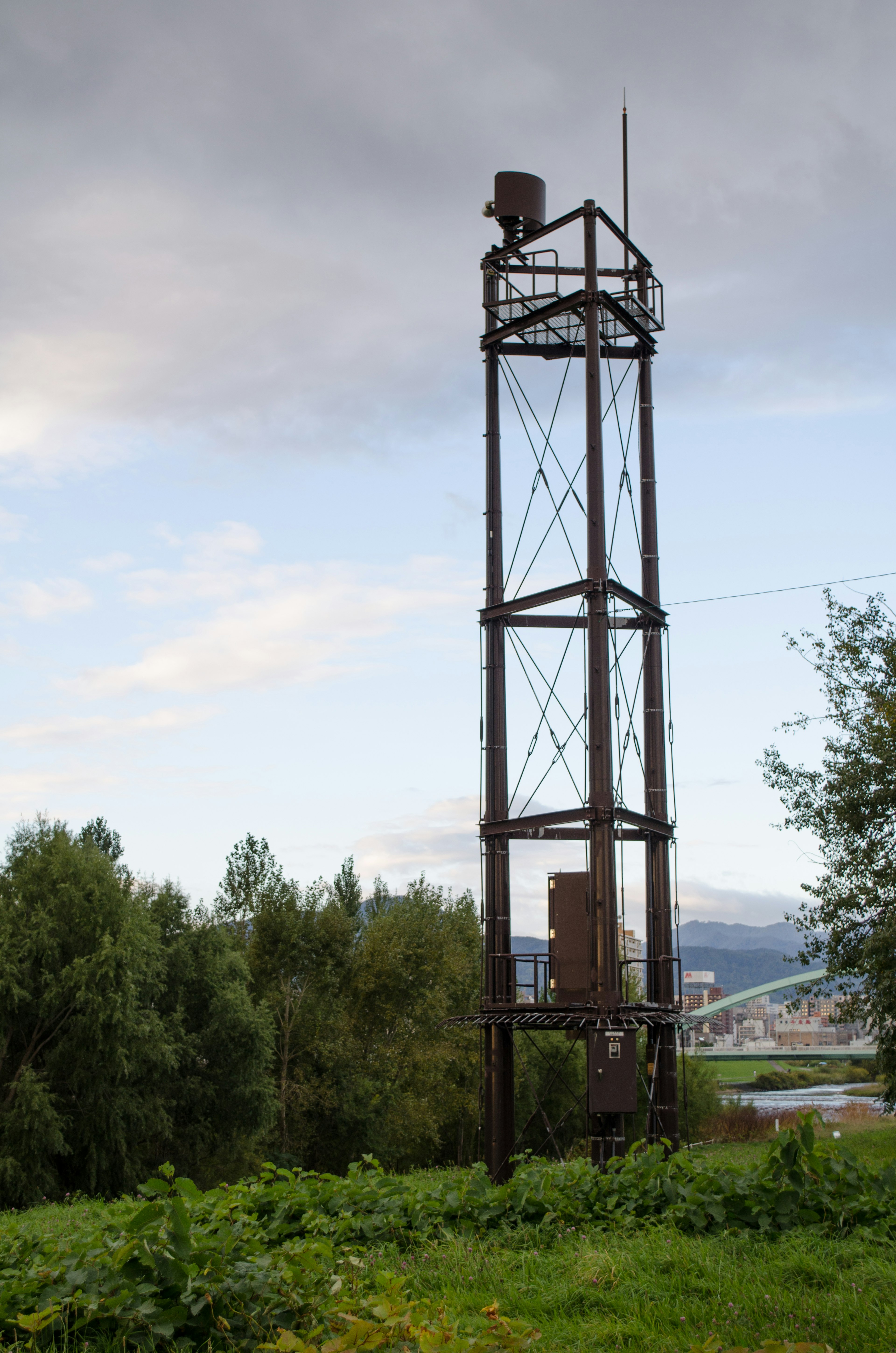 Torre metálica oxidada con un primer plano de césped verde y cielo nublado