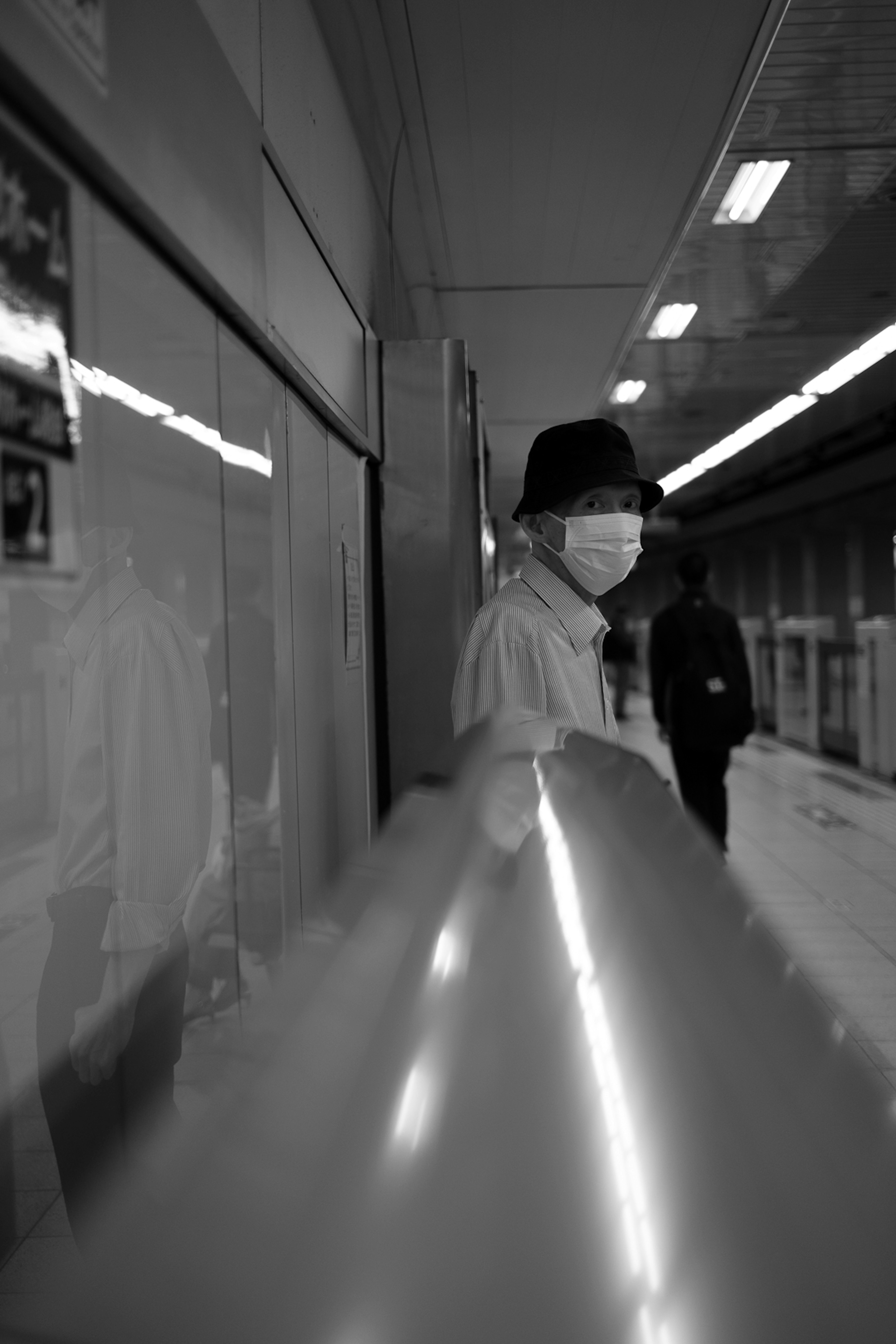 A person wearing a mask waiting at a subway station in black and white