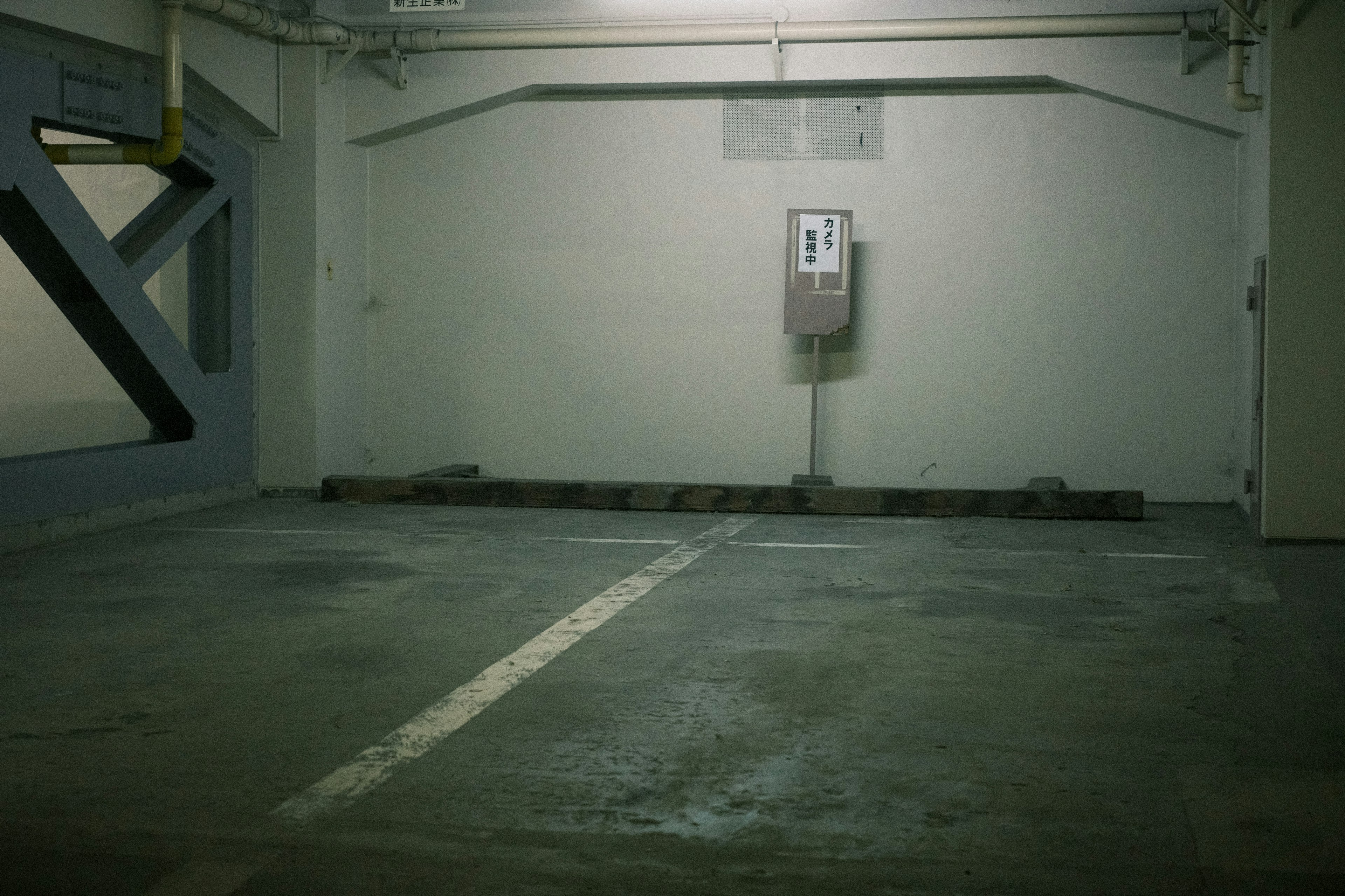 Empty parking lot corner with green walls and concrete floor featuring a single parking space and an old payment machine