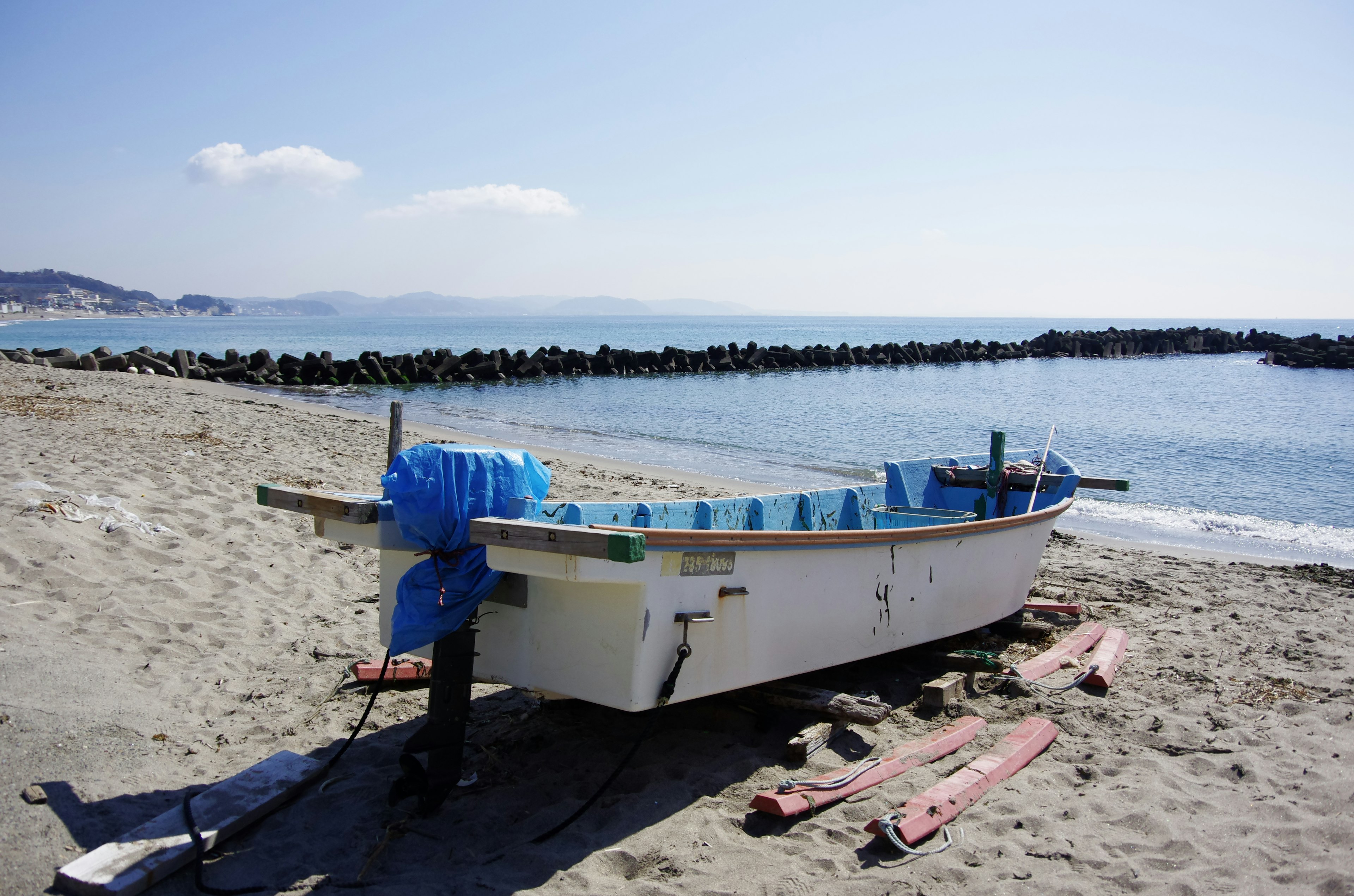 Barco de pesca blanco en la playa cubierto con una lona azul costa arenosa