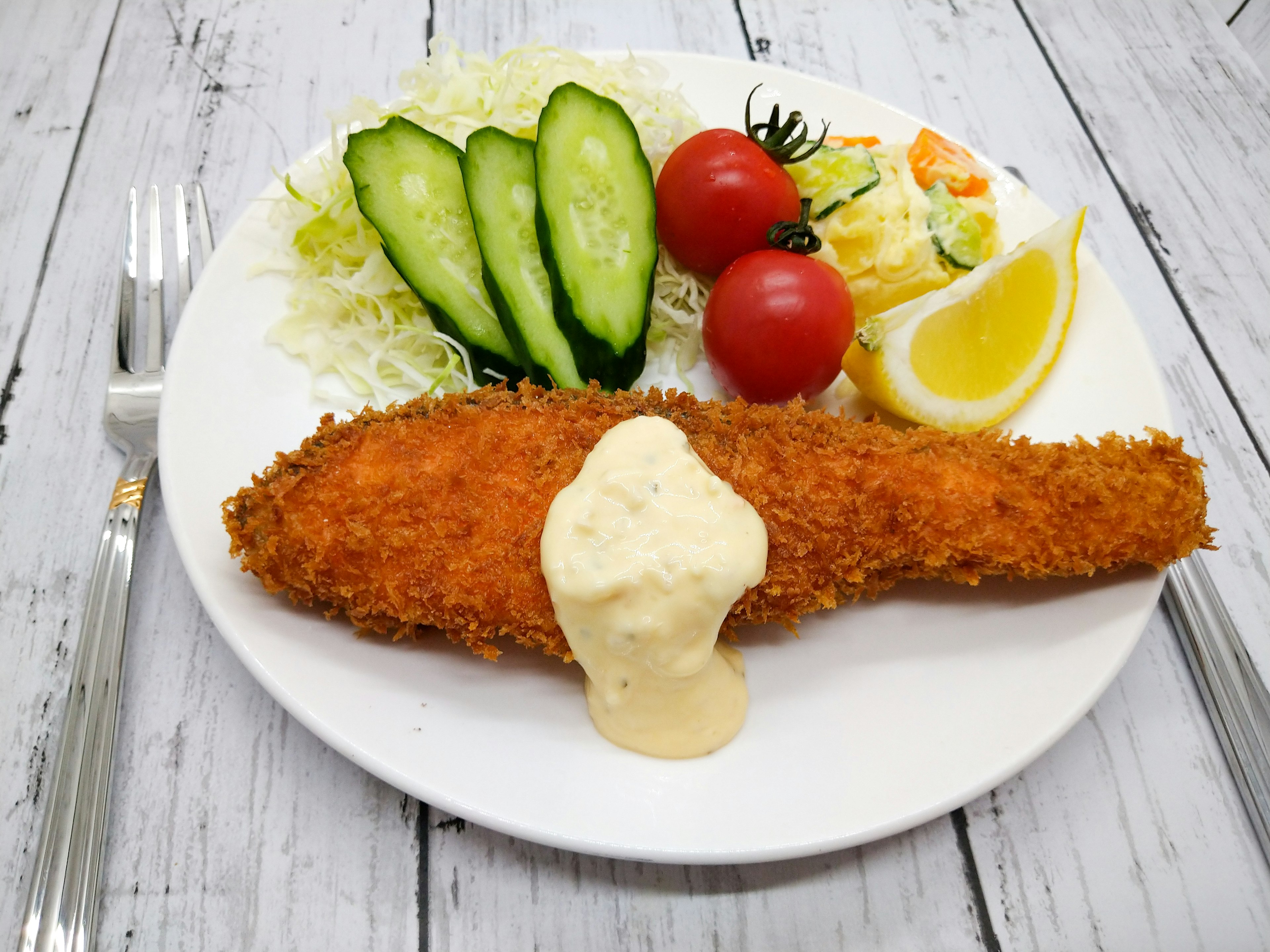 Pescado frito servido con ensalada, rodajas de pepino, tomates cherry y una rodaja de limón