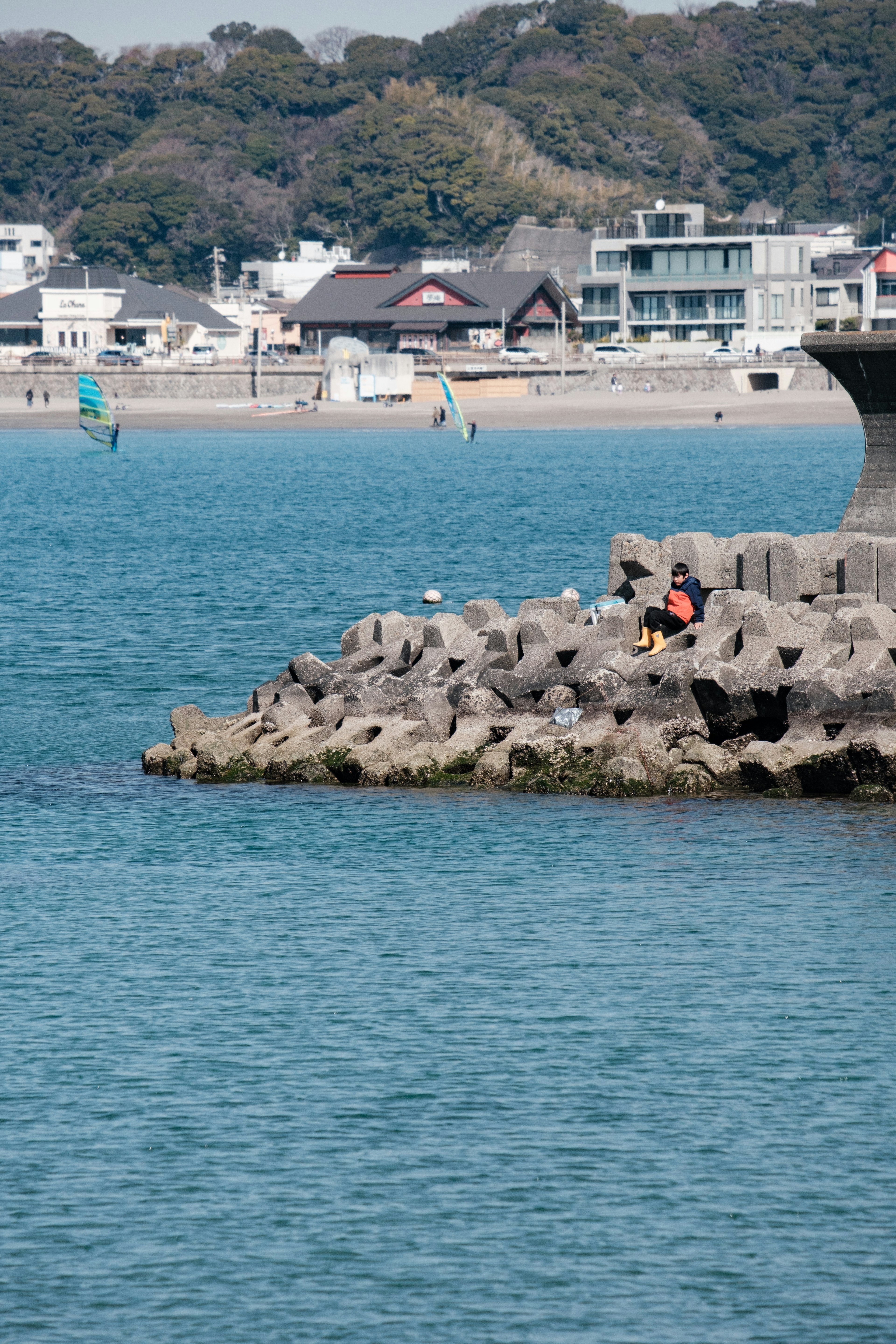 Personne assise sur une rive rocheuse avec de l'eau calme et des bâtiments au loin