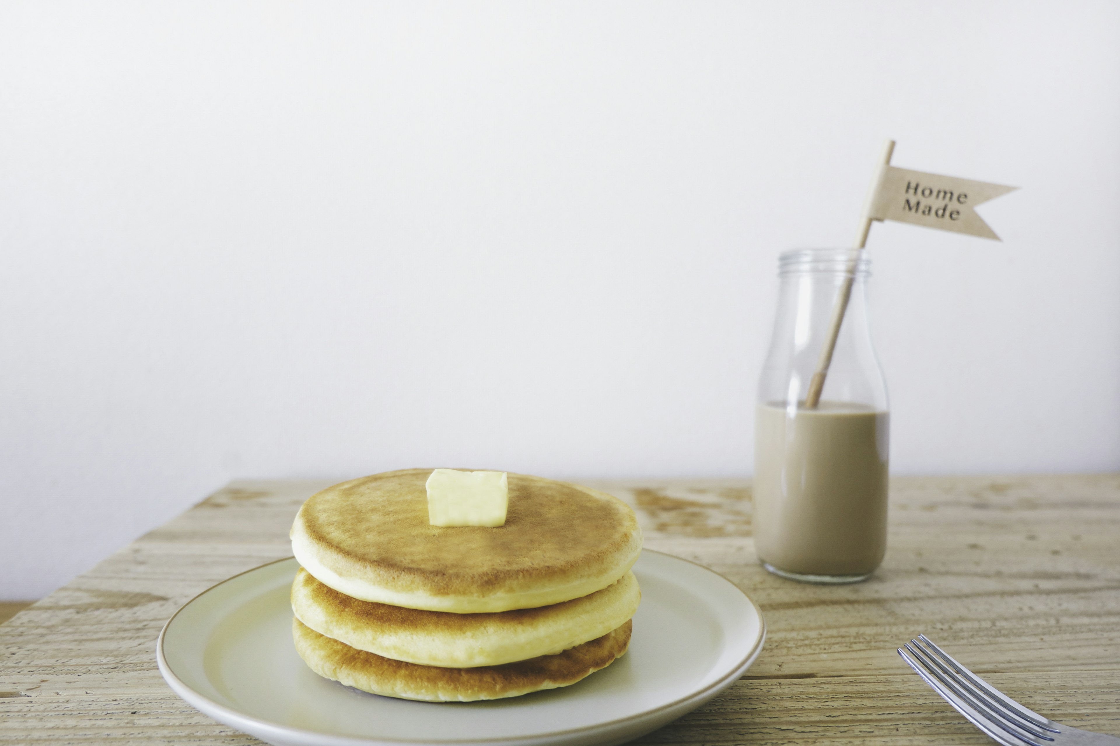 Tre pancake impilati con una noce di burro sopra e una piccola bandiera in una bottiglia di vetro