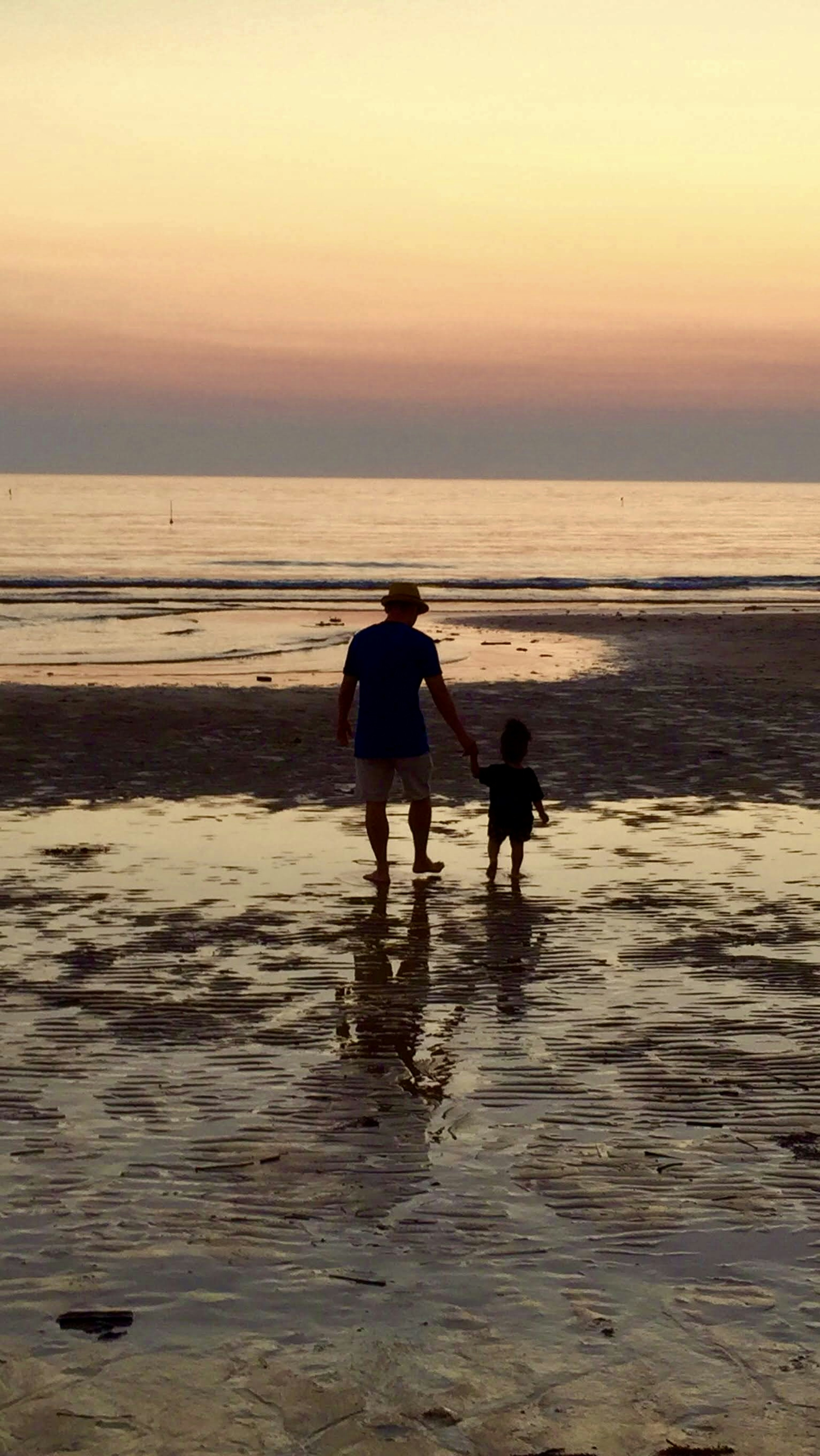 Silhouette d'un adulte et d'un enfant marchant main dans la main sur fond de coucher de soleil