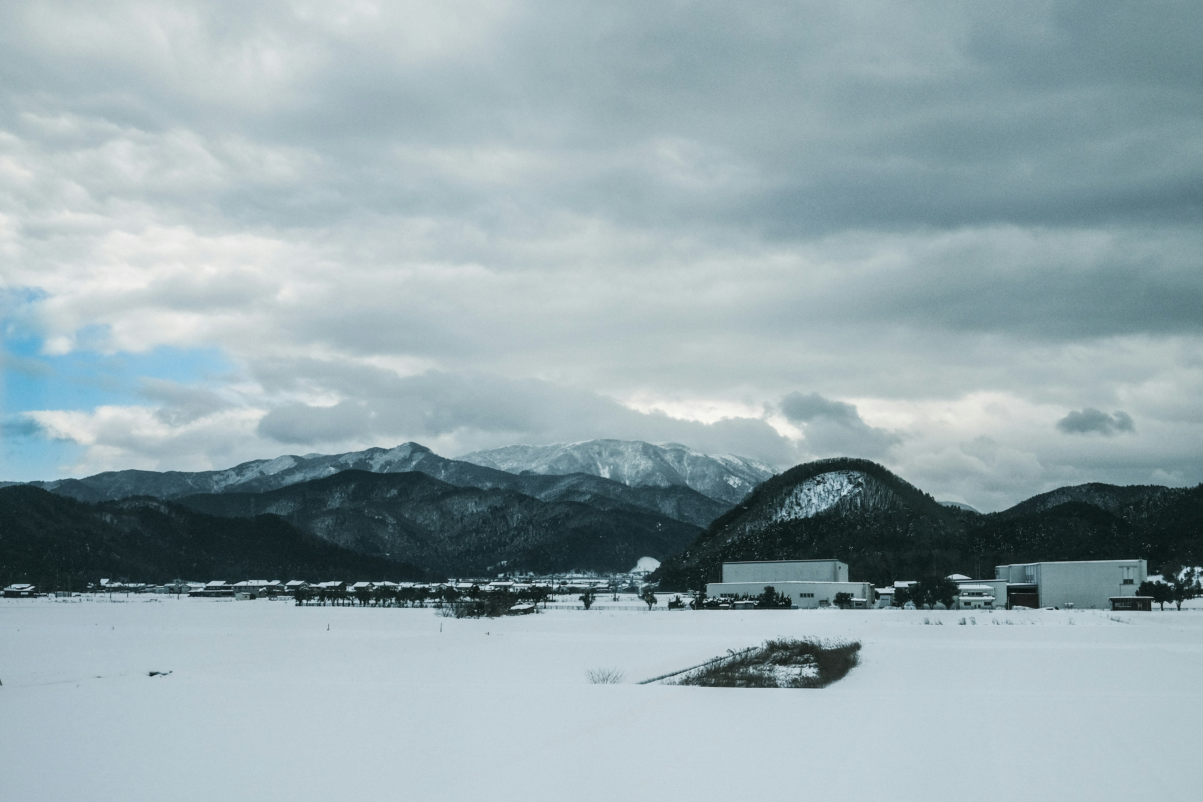 Llano cubierto de nieve con montañas al fondo y cielo nublado