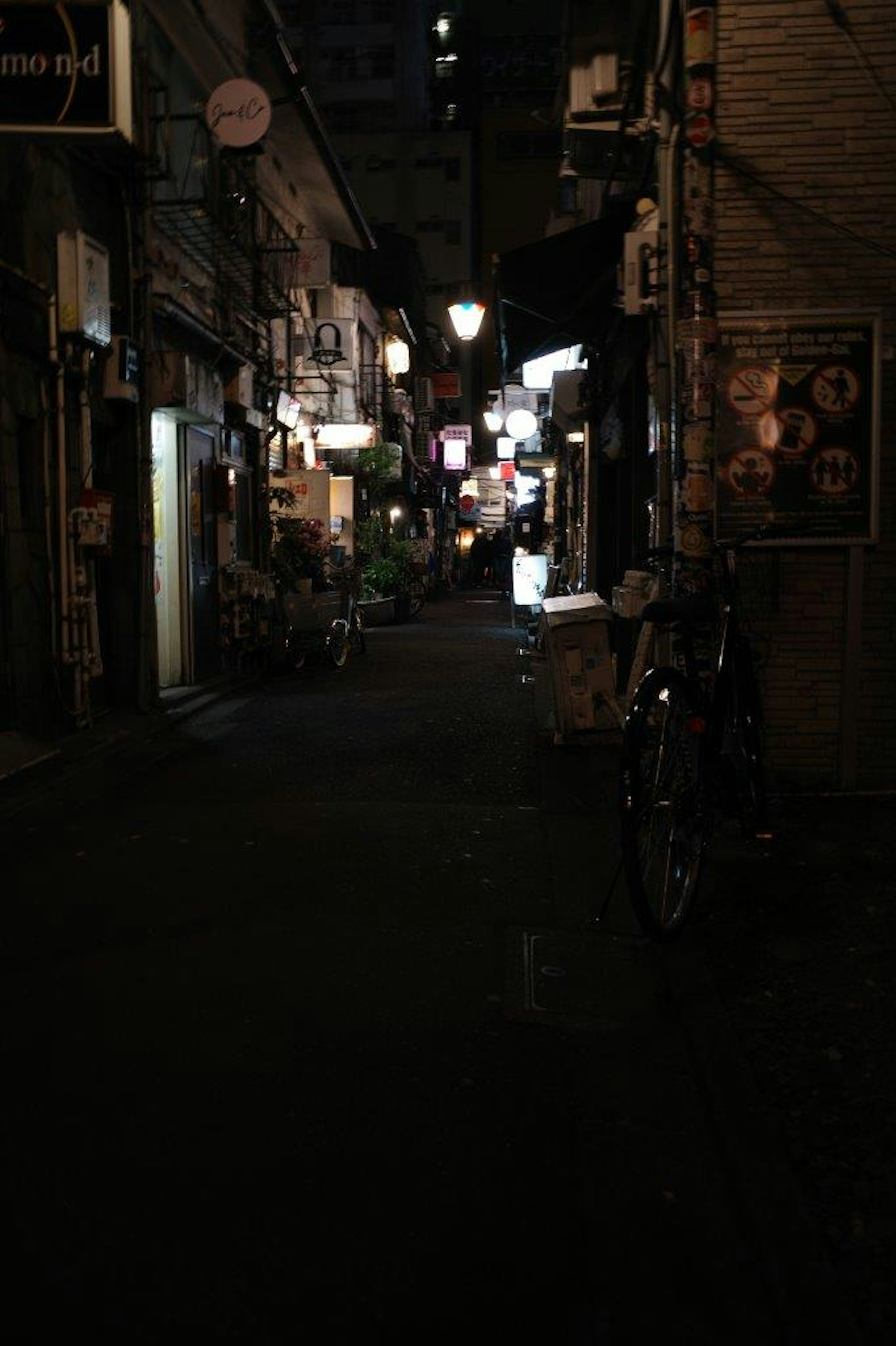 Narrow dark alley with illuminated restaurant signs and bicycle shadows