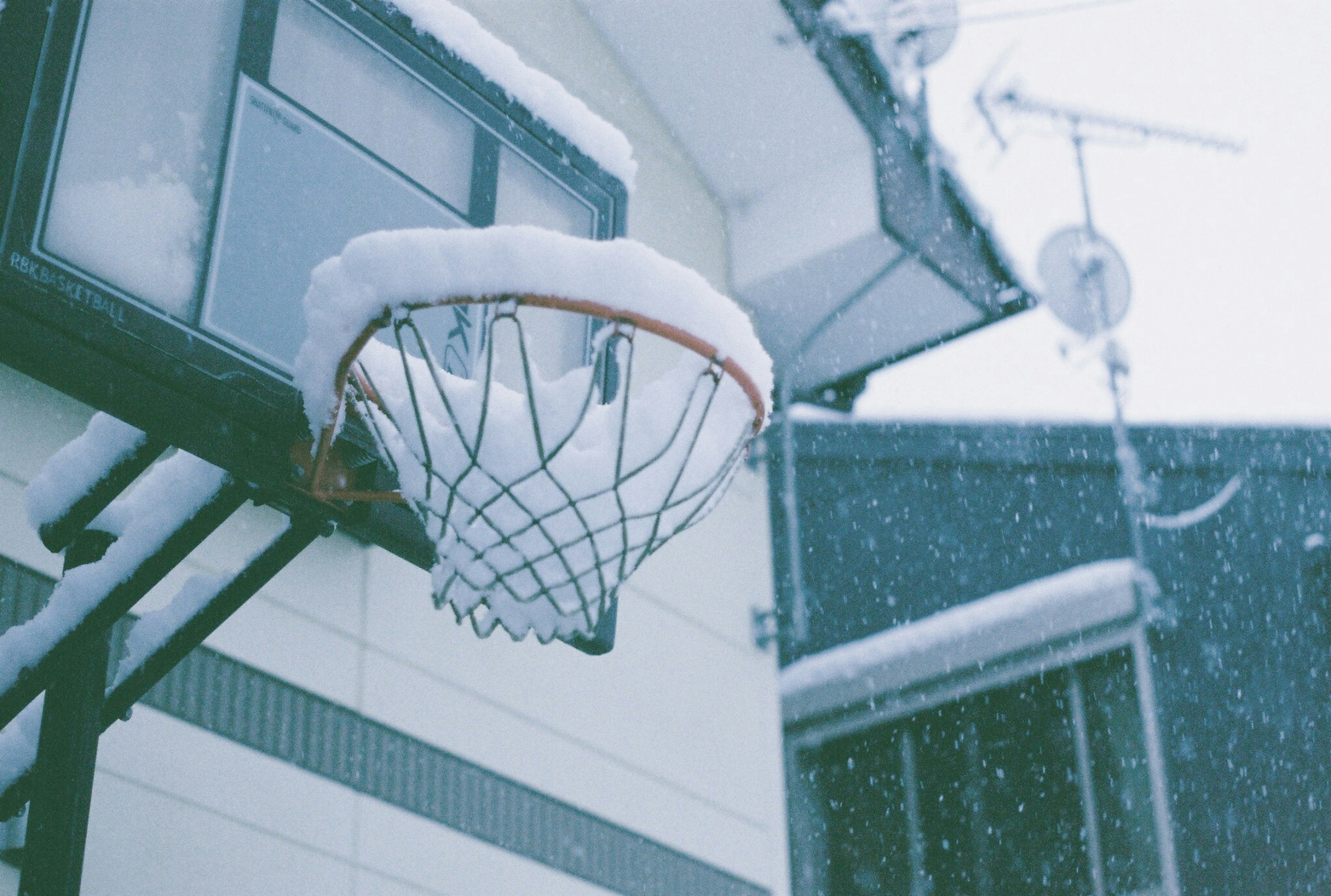 Basketball hoop covered in snow with a house in the background