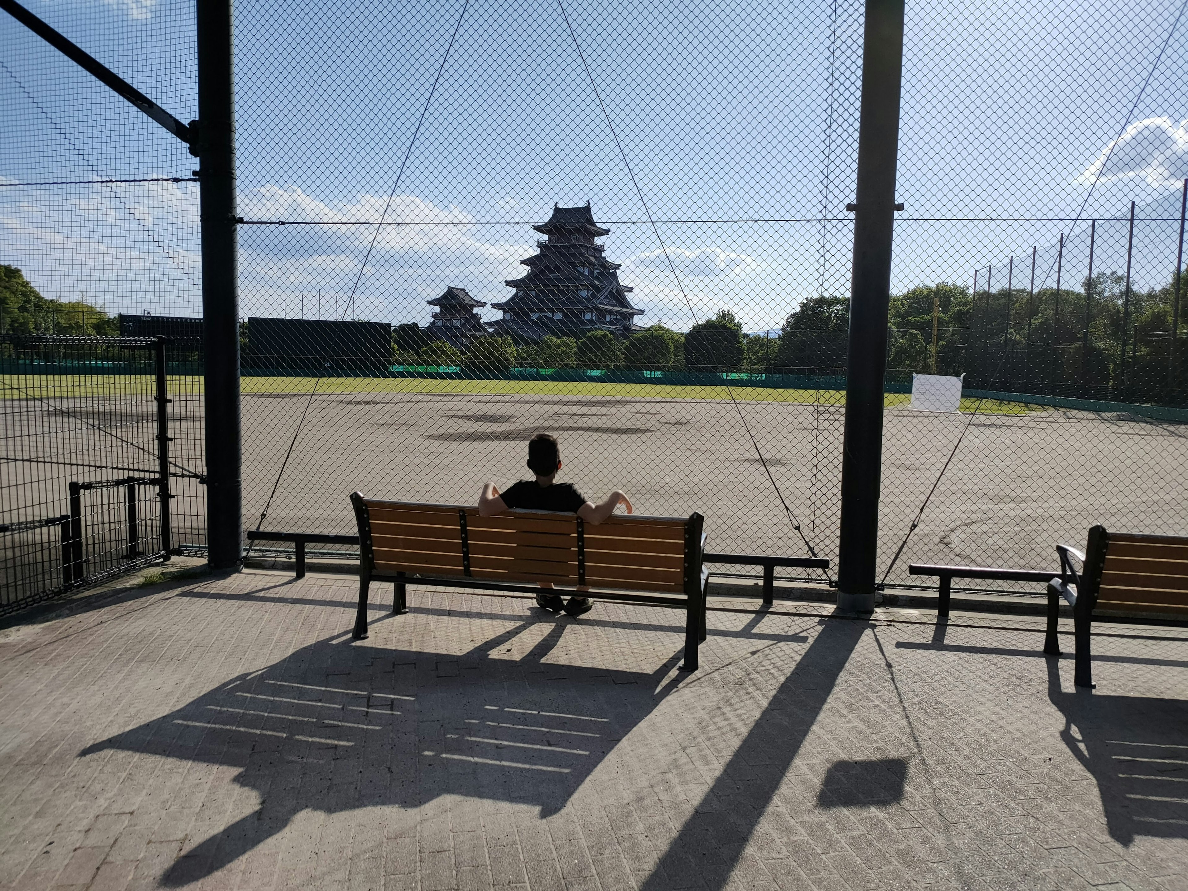 Una persona sentada en un banco con vista a un campo de béisbol y un castillo al fondo