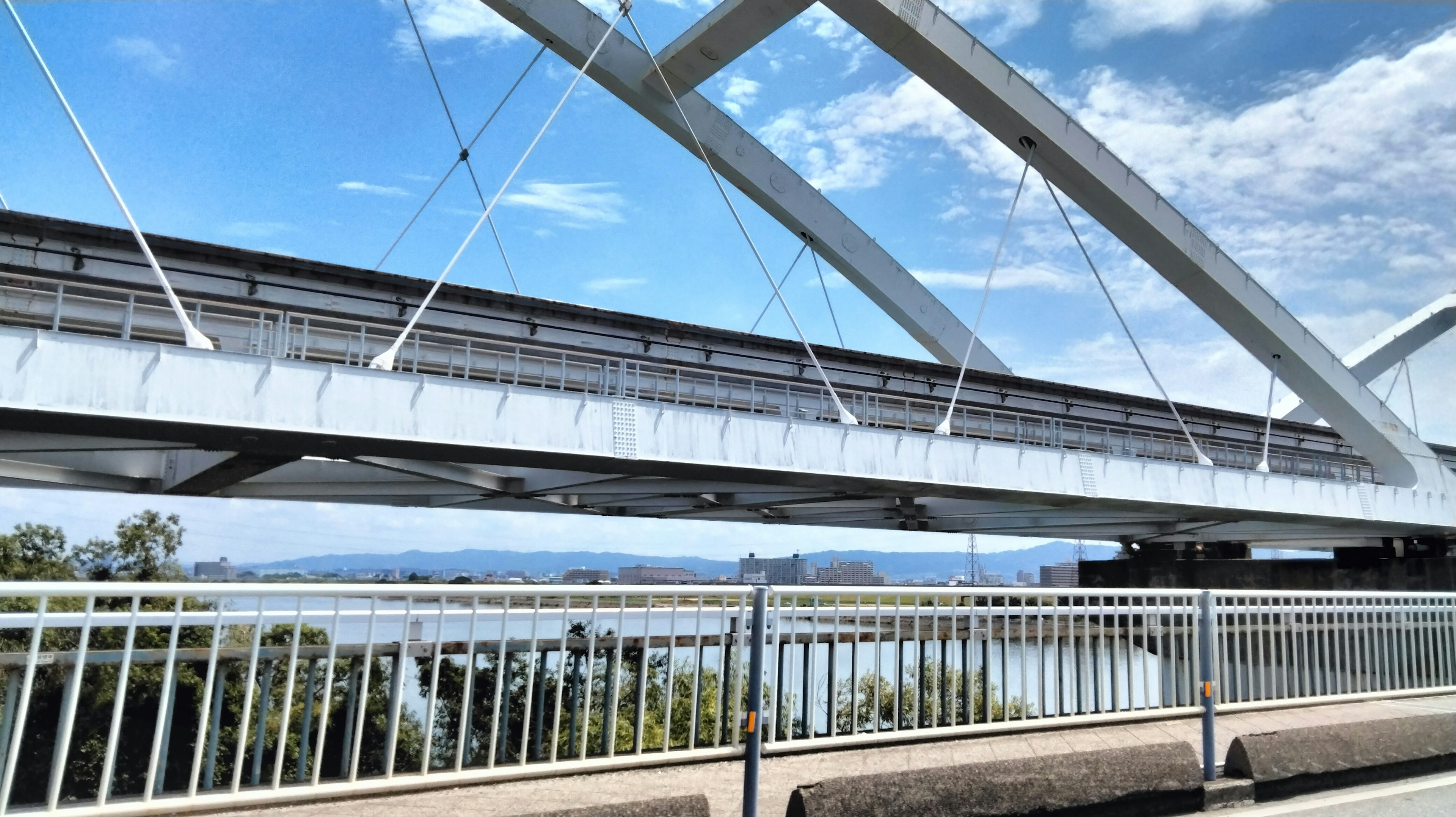 Jembatan baja modern di bawah langit biru dengan vegetasi di sekitarnya