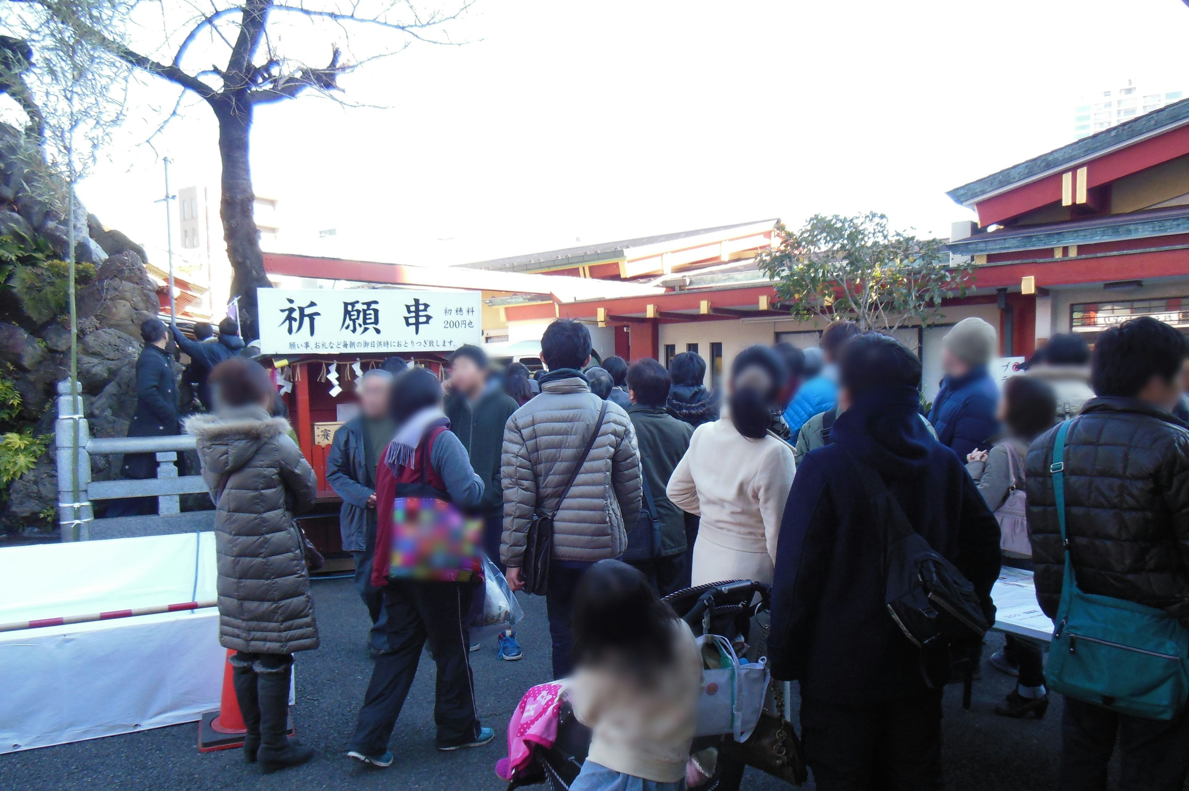 Crowd of people waiting at a shrine with a red building in the background