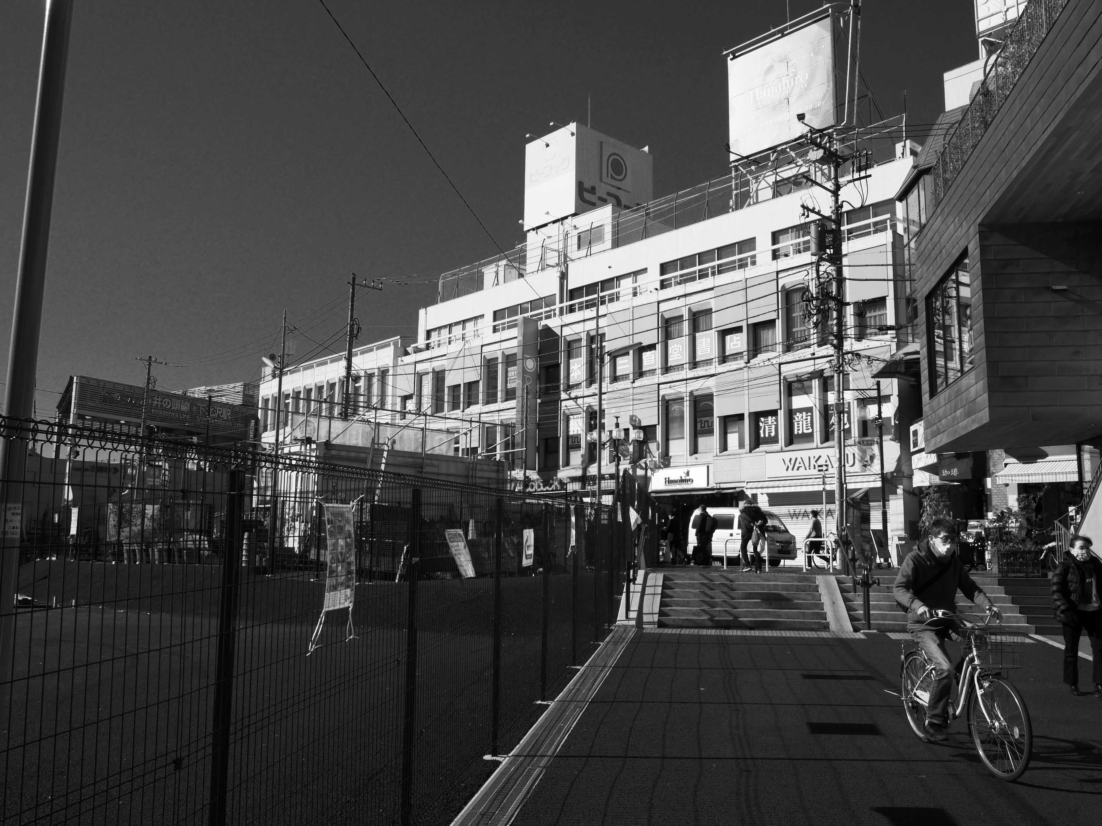 Scène urbaine en noir et blanc avec un cycliste et des bâtiments présentant une façade de gare moderne