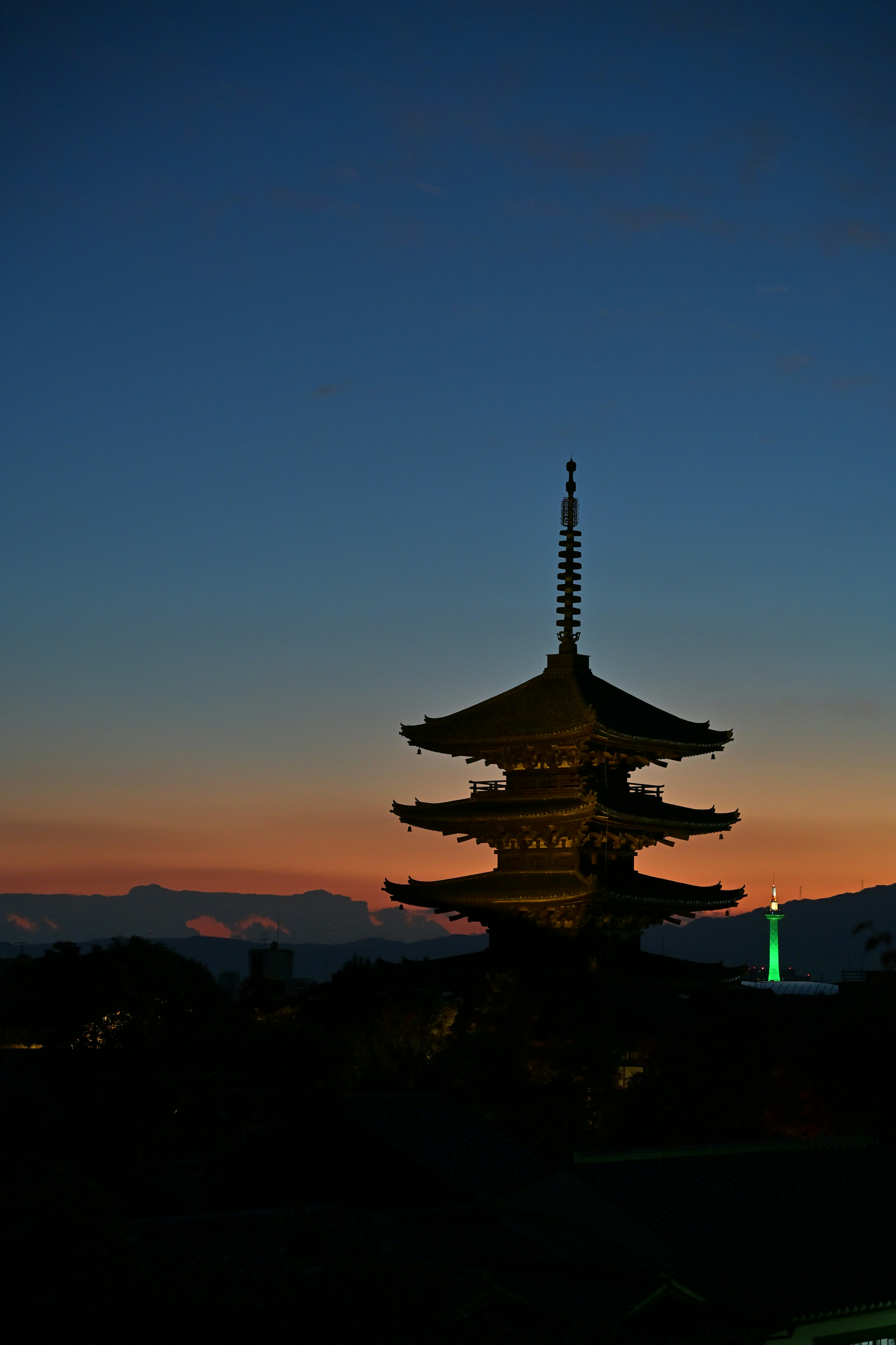 Silhouette di una pagoda contro un tramonto colorato con montagne sullo sfondo