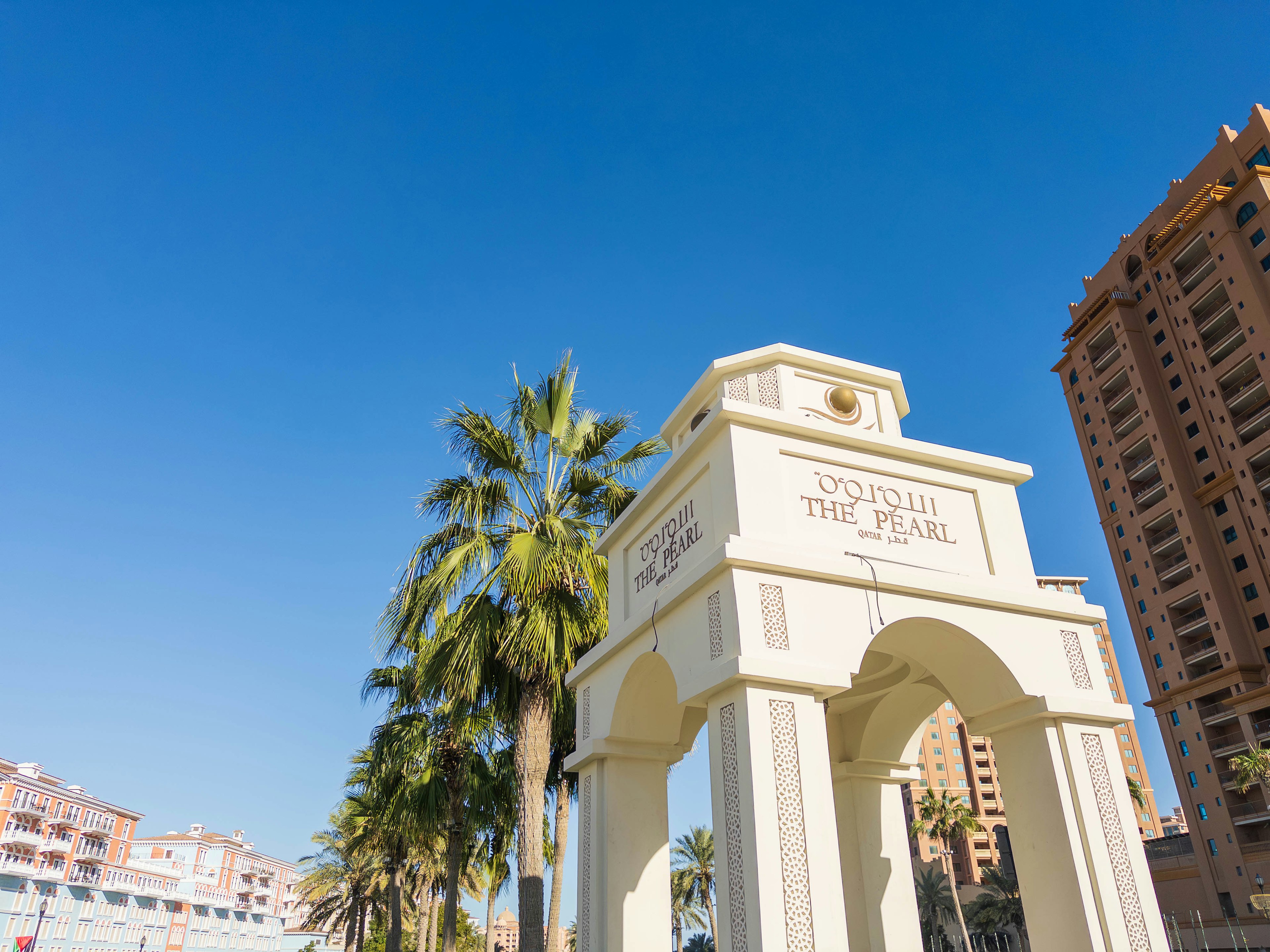 White arch under a clear blue sky with palm trees