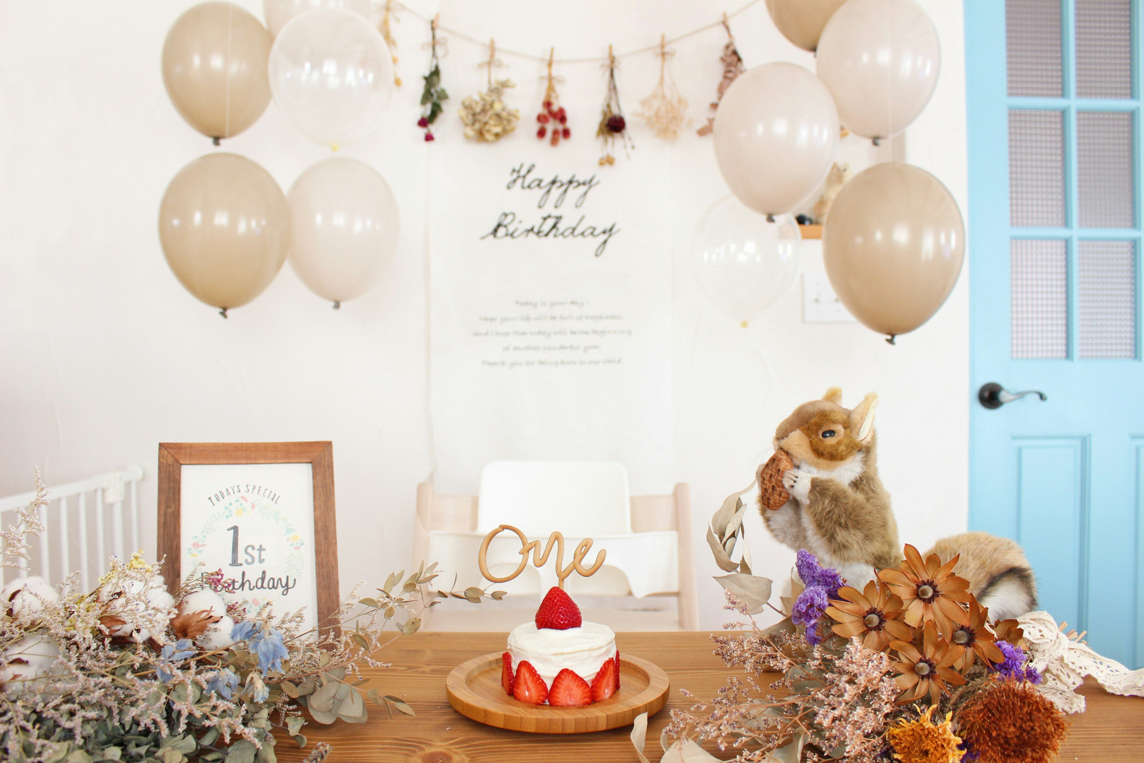 A birthday decorated table featuring a cake with strawberries and balloons, with a 'Happy Birthday' backdrop