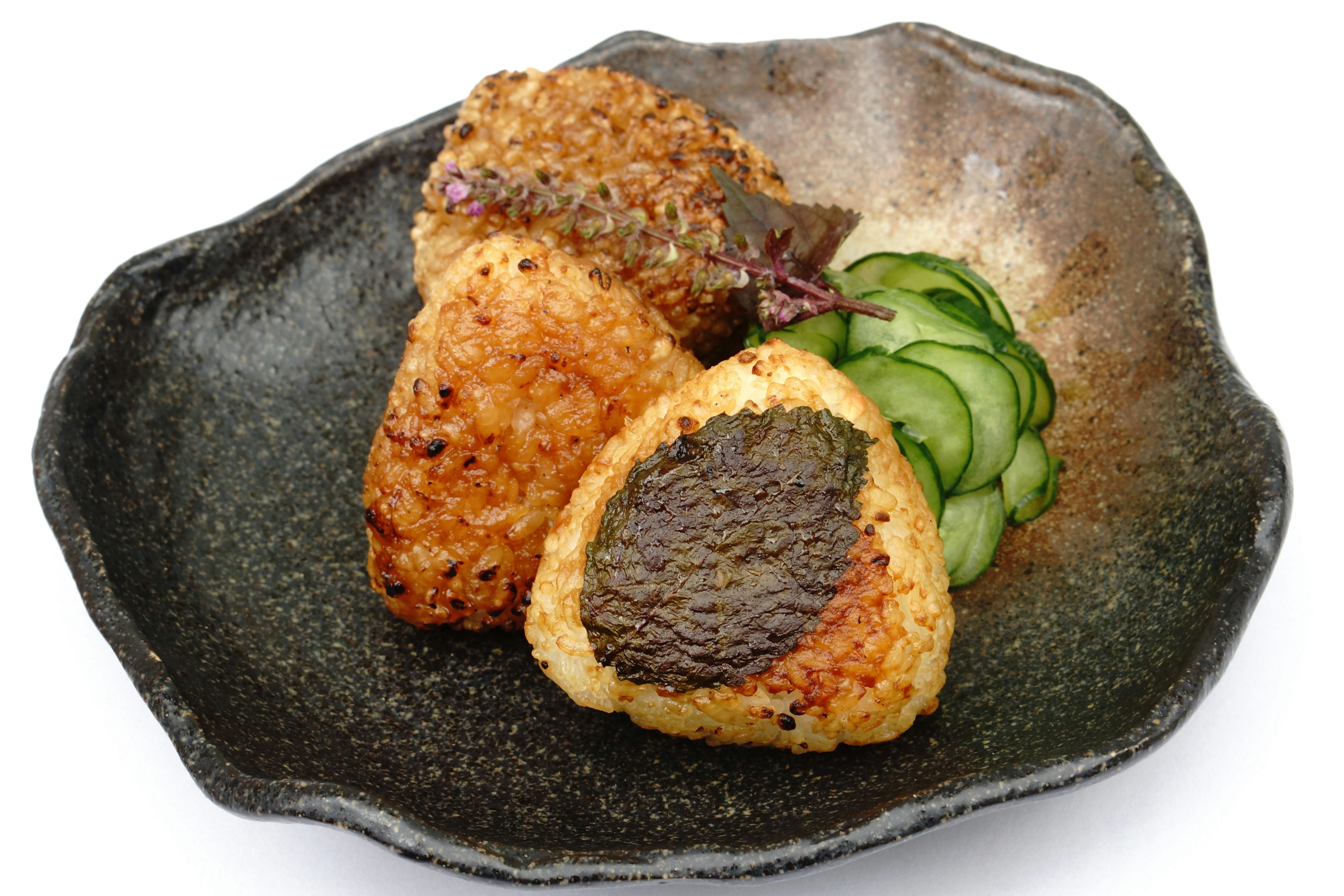 Two grilled rice balls served on a black plate with sliced cucumbers