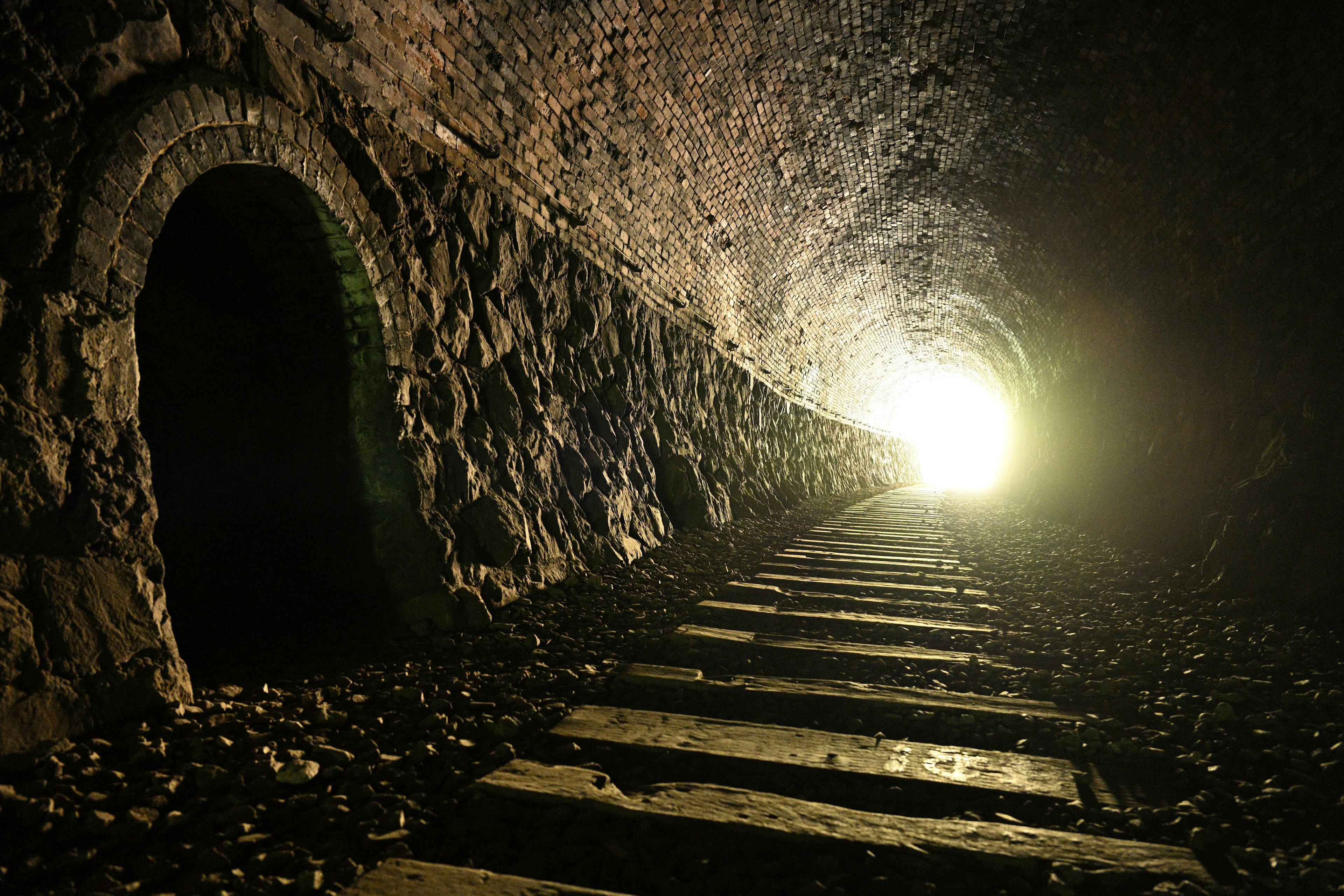 Innenseite eines Steintunnels mit einem Holzboden, der zu einem hellen Licht am Ende führt