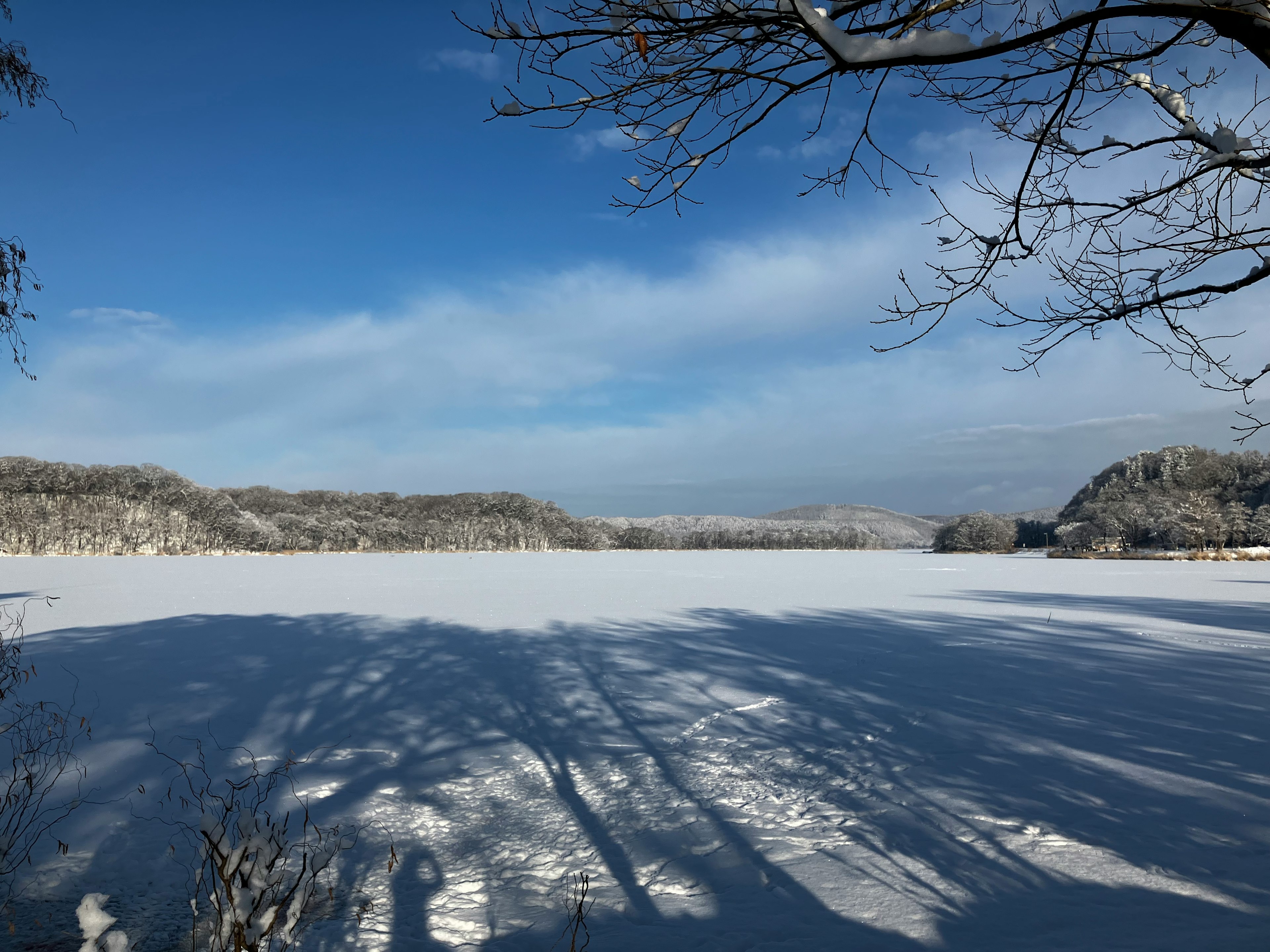 Lago coperto di neve con cielo blu e colline in lontananza