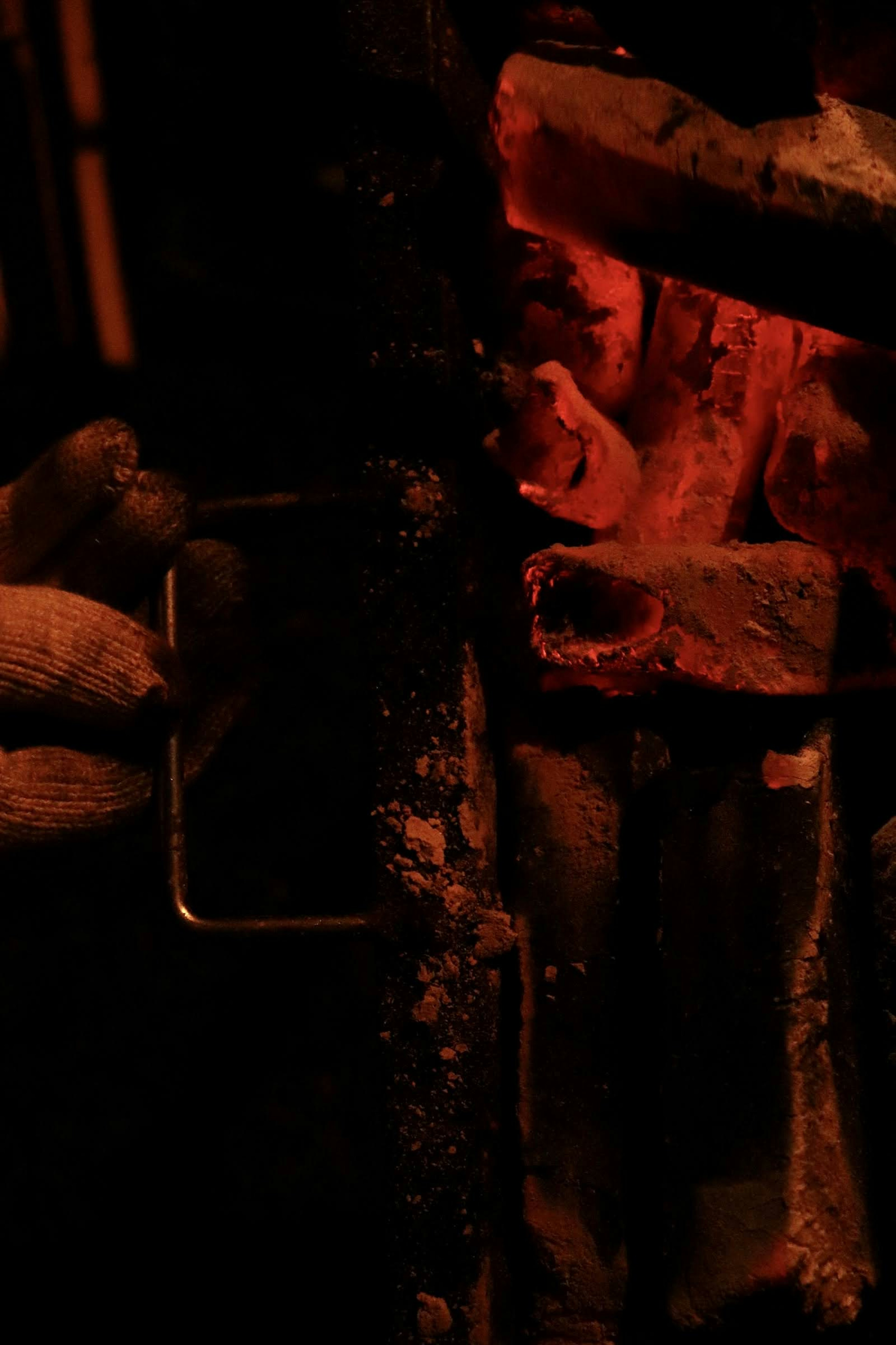 A hand holding a metal tool near glowing embers and flames