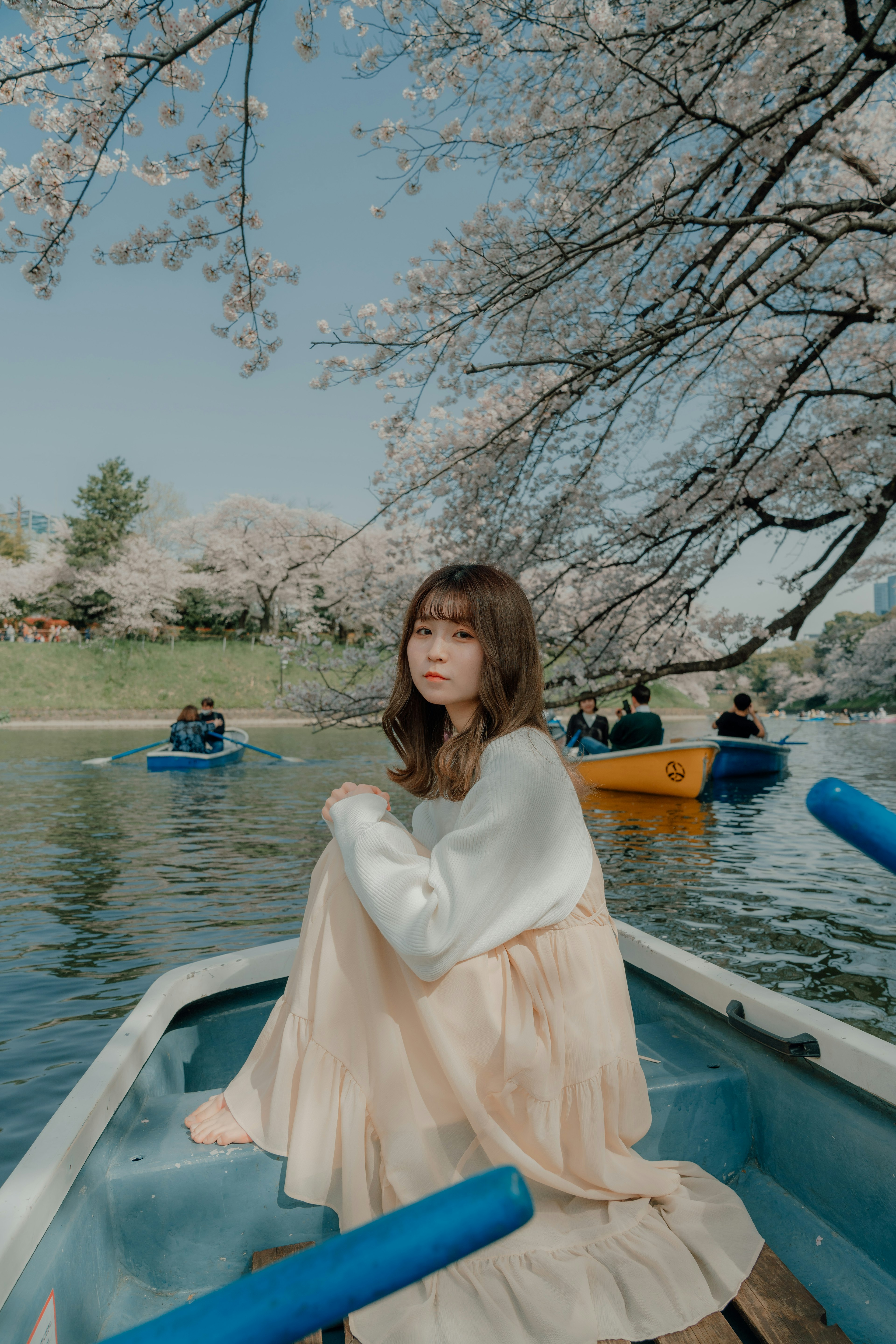 A woman sitting in a boat under cherry blossom trees