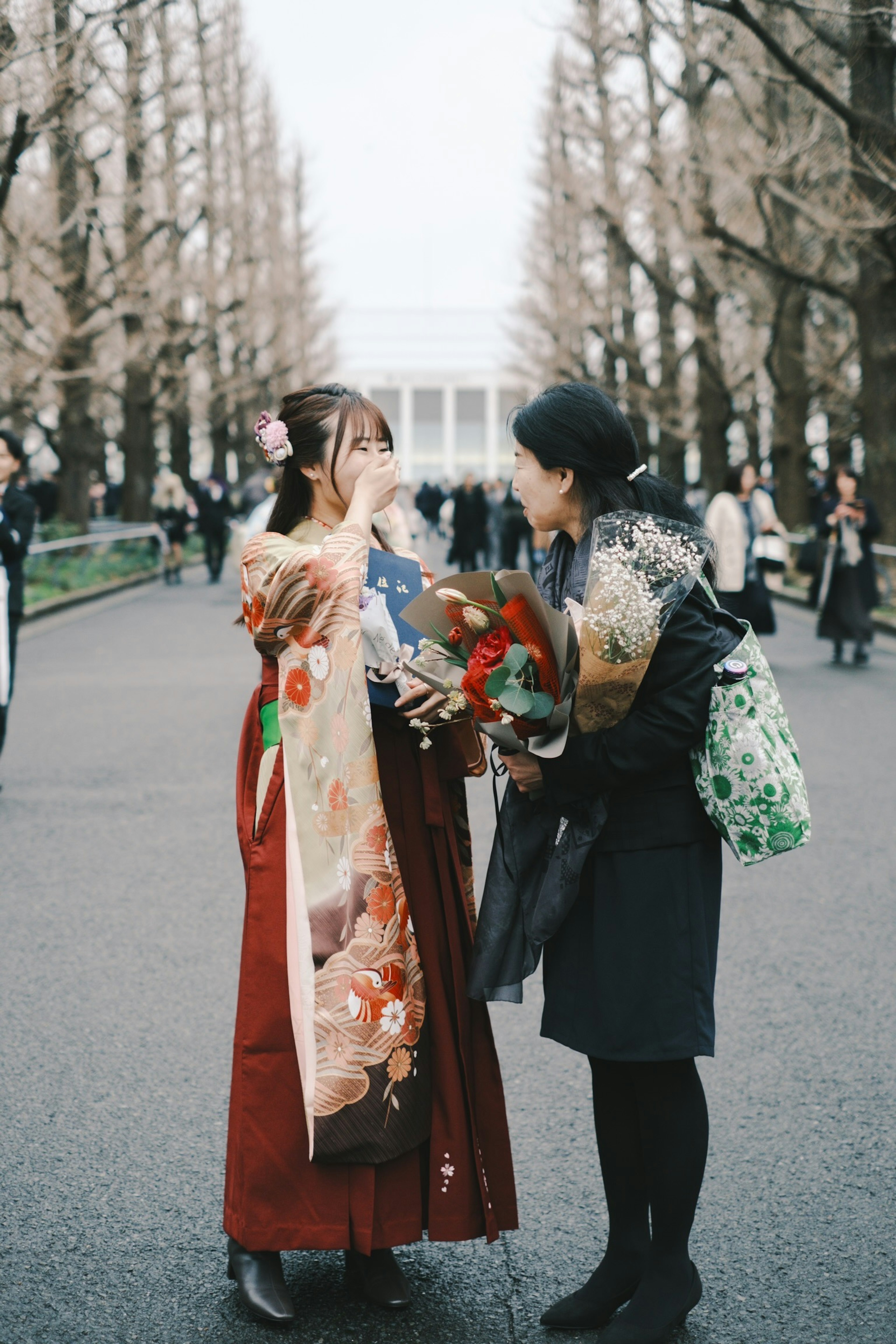 Two women standing together on a tree-lined path engaged in conversation