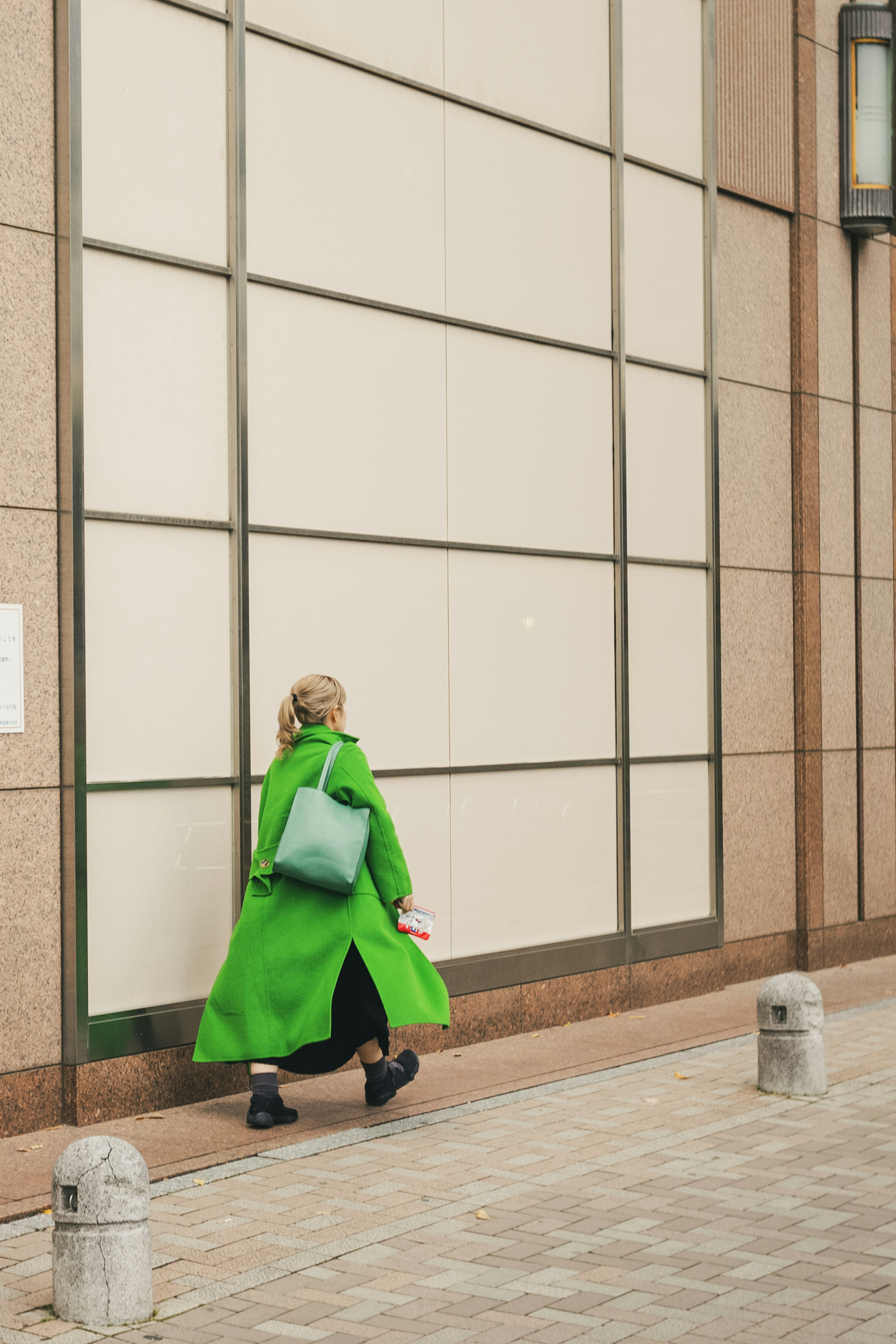 Une femme en manteau vert marchant le long d'un mur de bâtiment