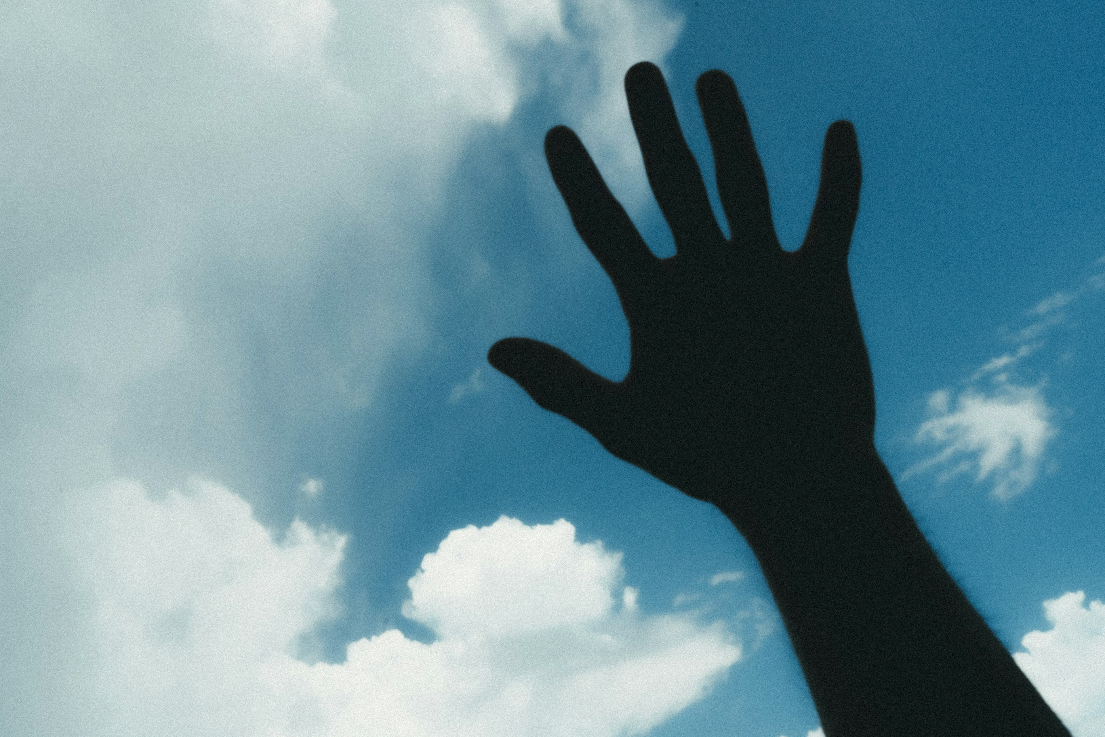 Silhouette of a hand reaching out against a blue sky