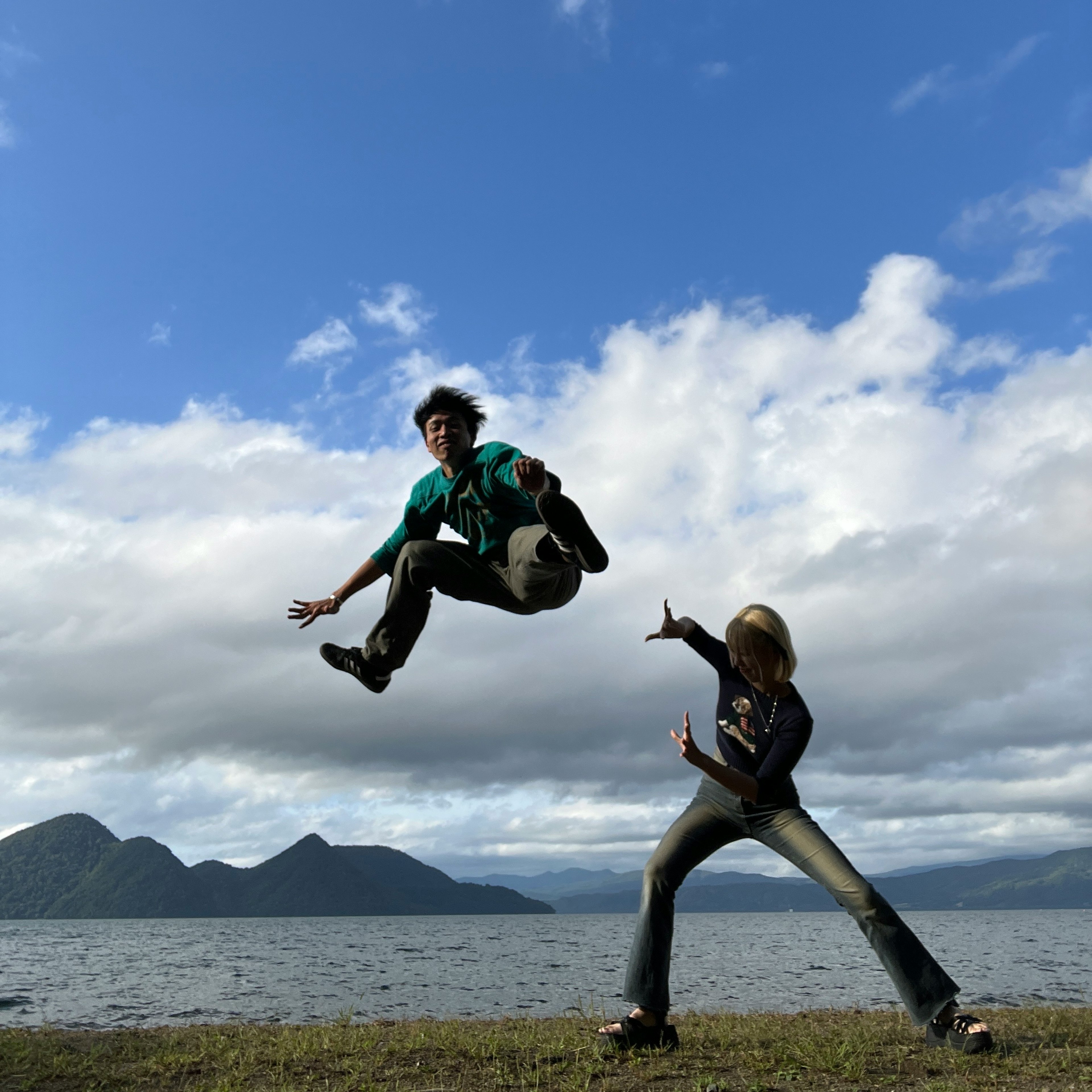 湖のほとりでジャンプする男性とポーズを取る女性の写真